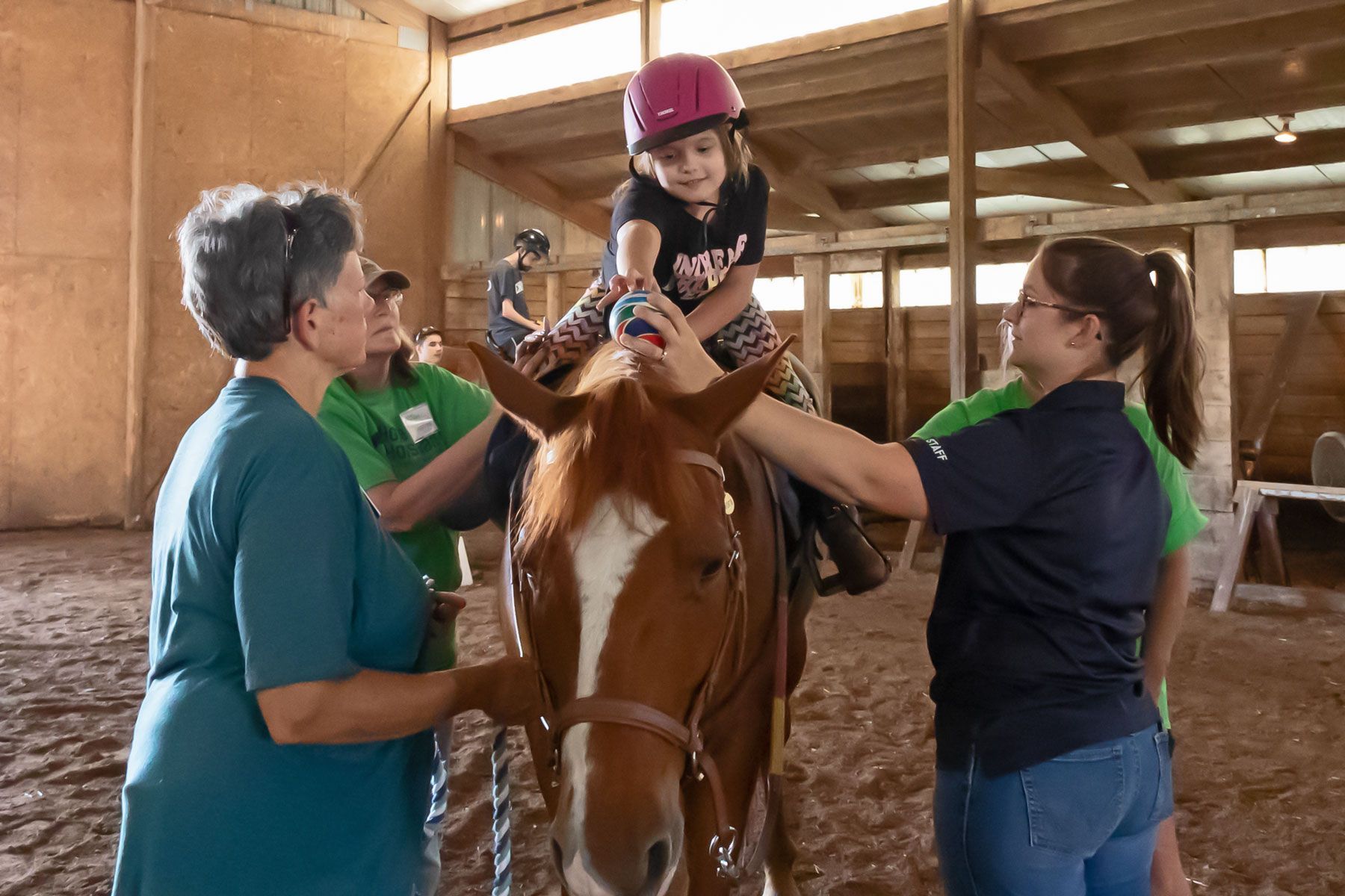 Children and adults help a rider on a horse inside a wooden stable
