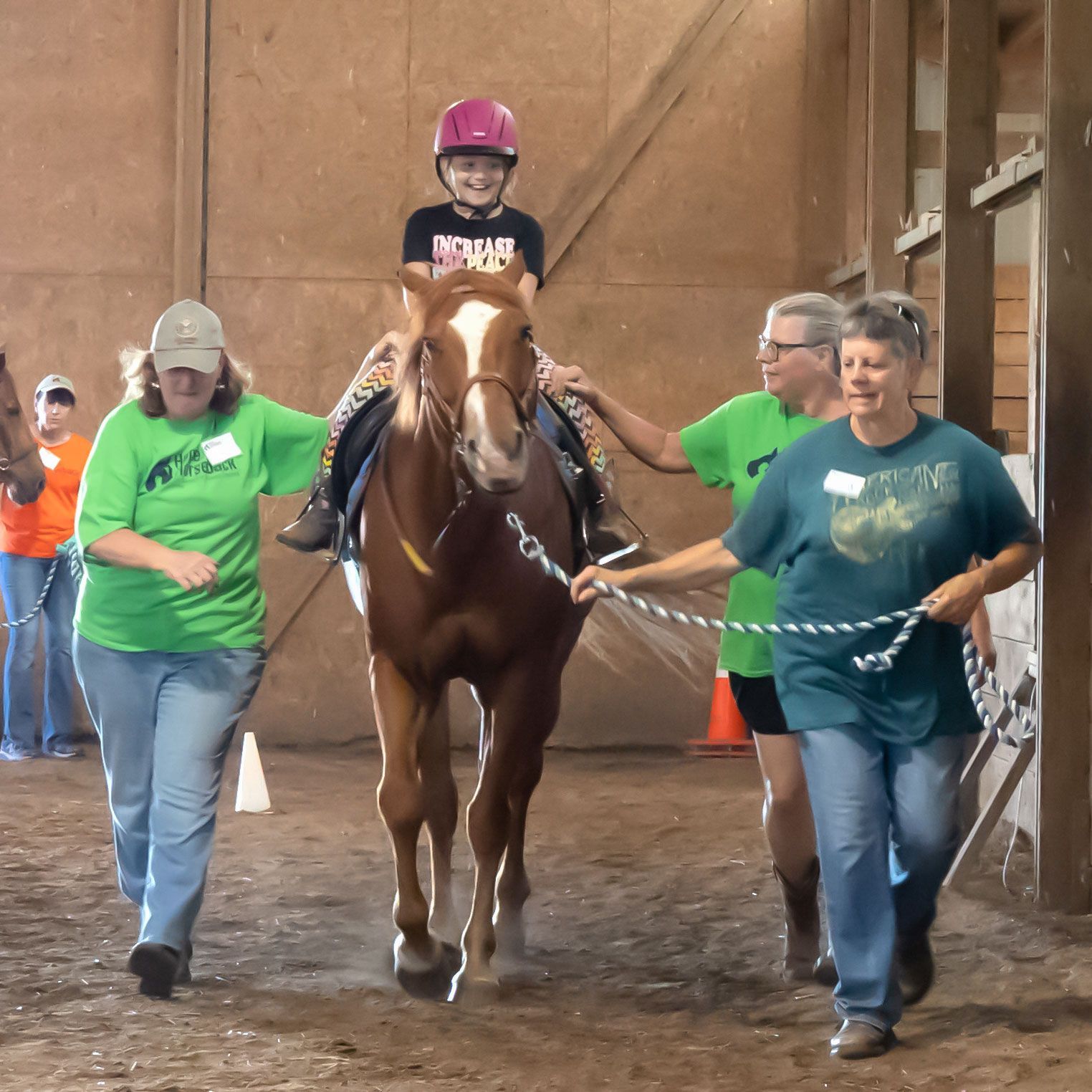 Child riding a horse indoors, guided by two adults holding leads
