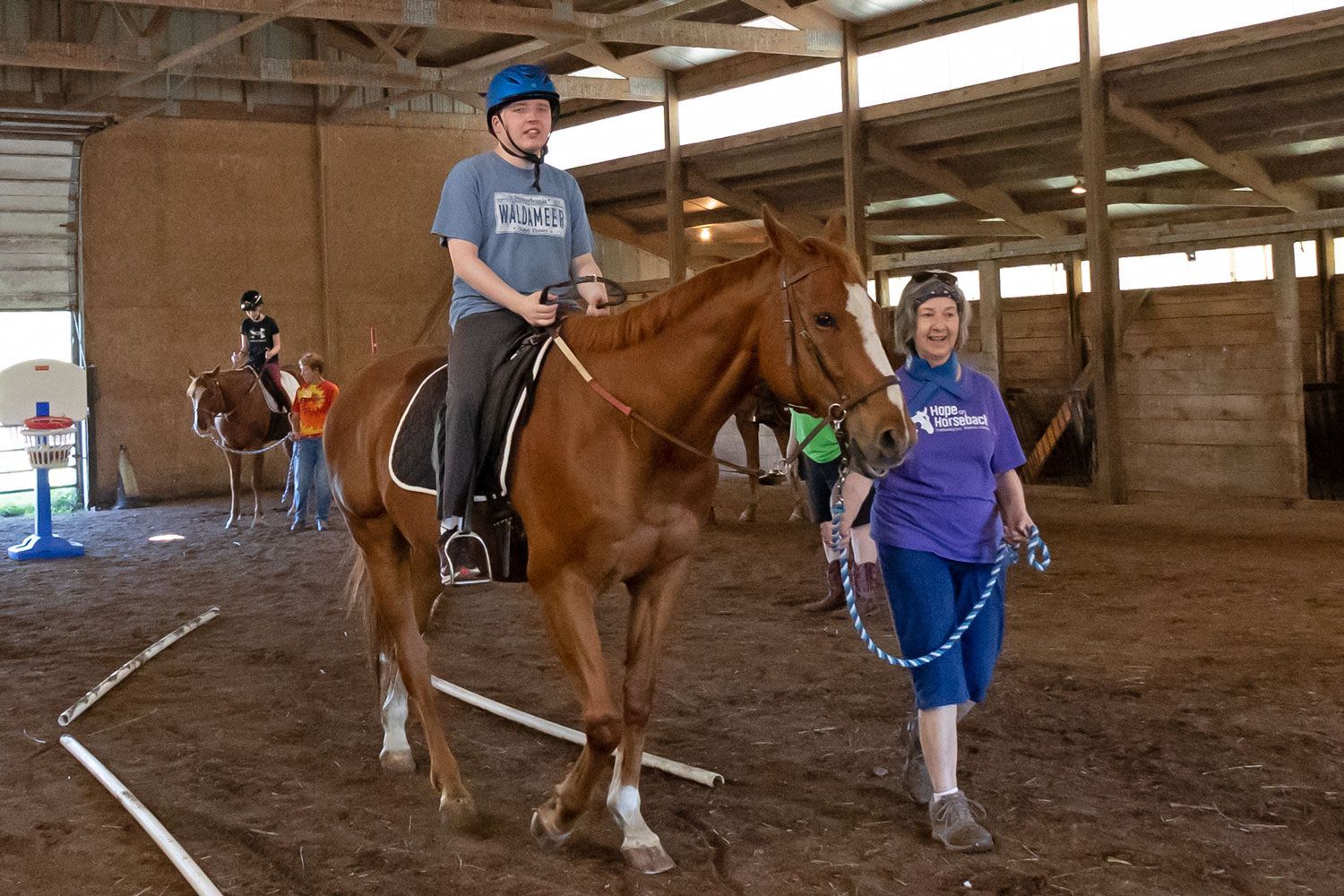 Young rider on a brown horse being led in an indoor riding arena