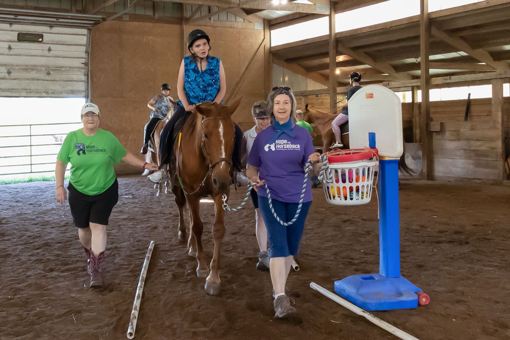 Three people leading a horse indoors in an arena, with a child riding on top.