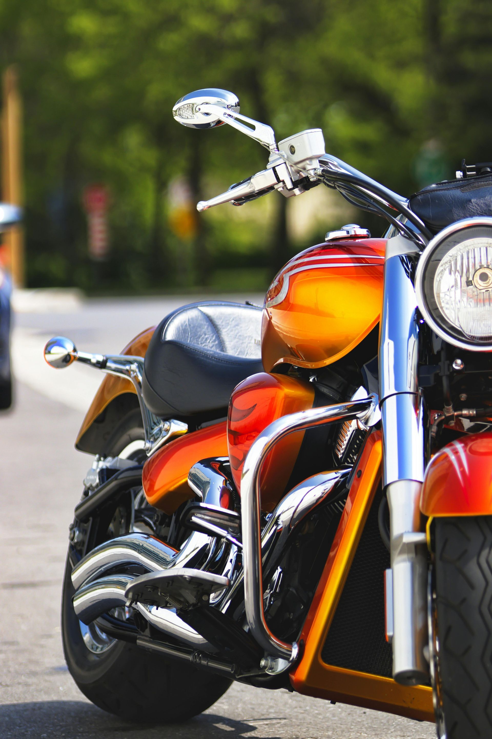 Chrome and orange motorcycle parked on a street with a blurred green background
