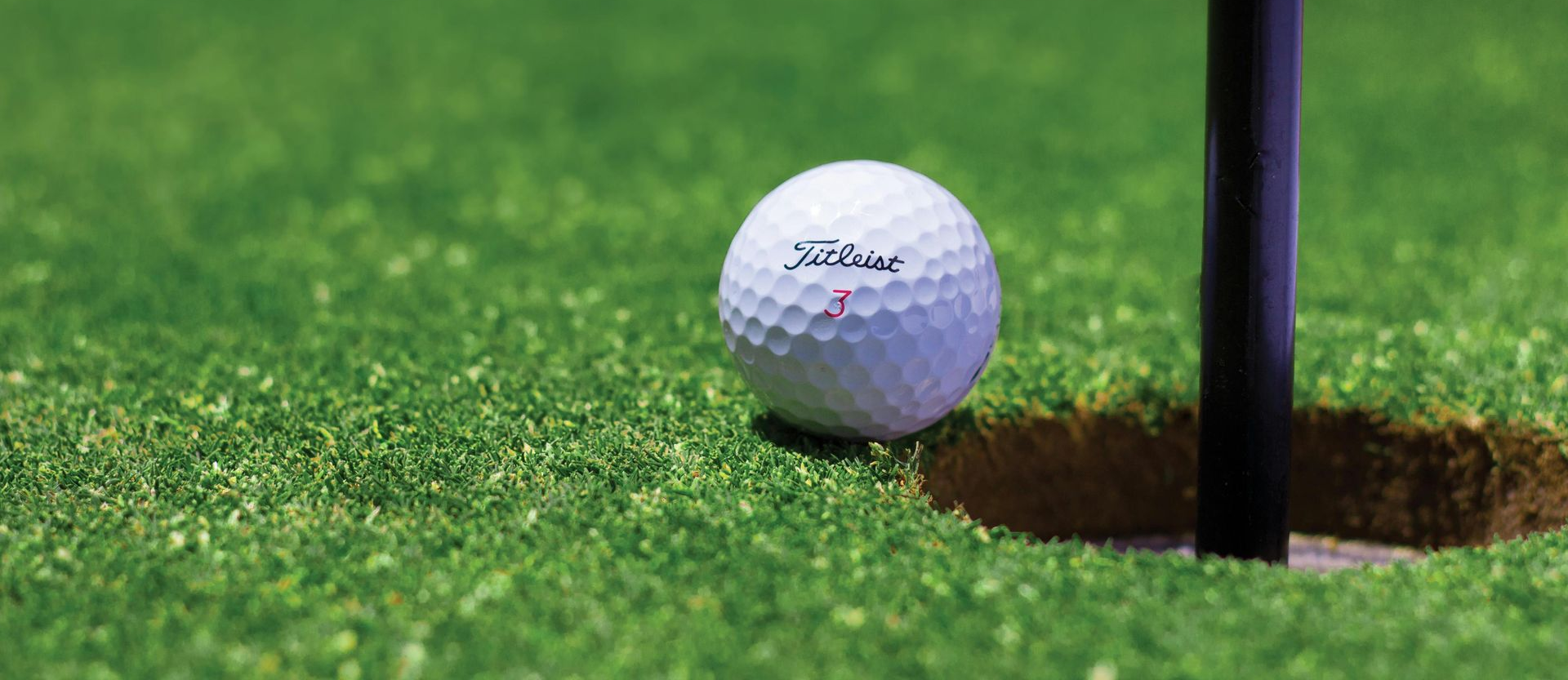 Golf ball beside a hole on green grass near a black flagstick