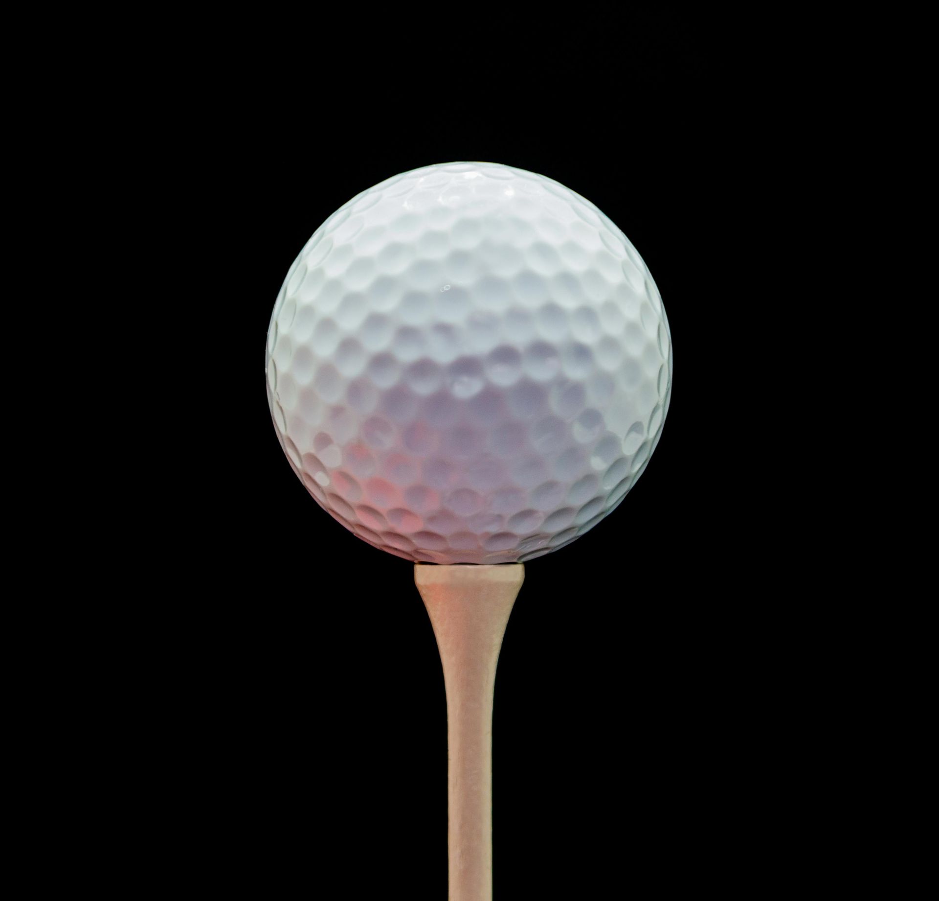 White golf ball perched on a wooden tee against a black background