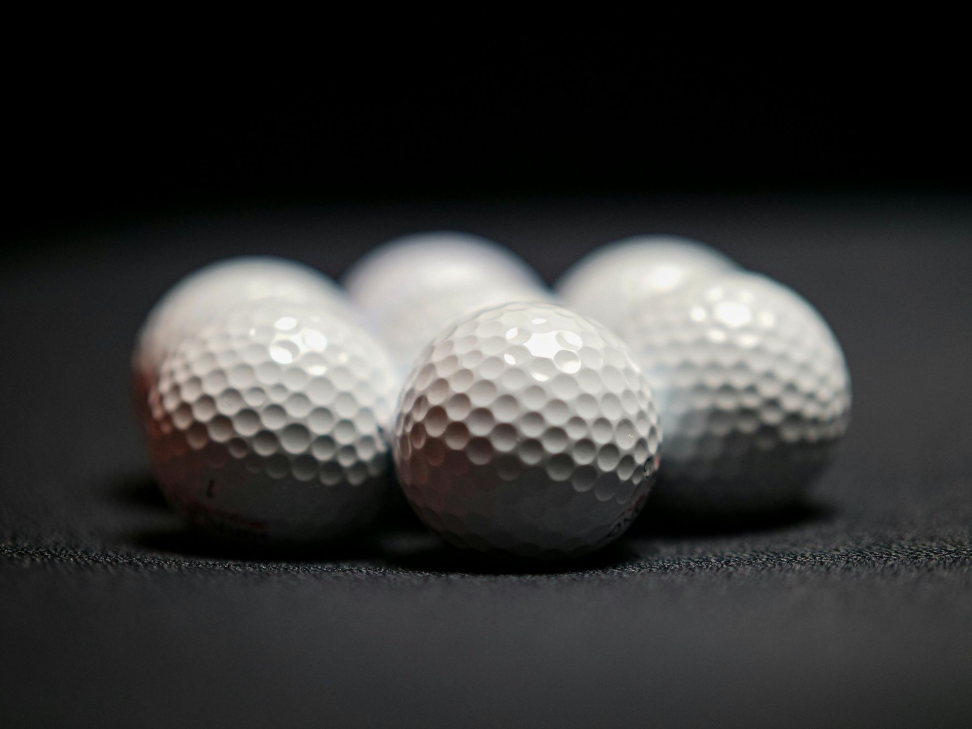Four white golf balls on a dark surface, lit against a black background