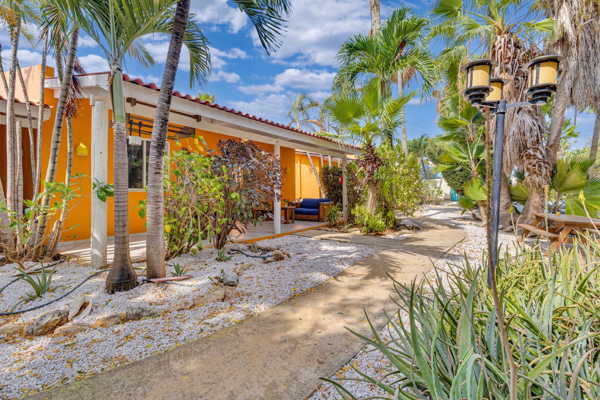 Yellow building with walkway and palm trees under a blue sky.
