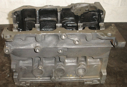 Bloque motor, fundición de metal gris, con cuatro aberturas de cilindros visibles, interiores negros.