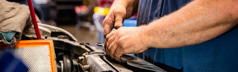 Mechanic working on a car engine, hands visible. Air filter, red tools, and blue shirt present. | Rick's Automotive