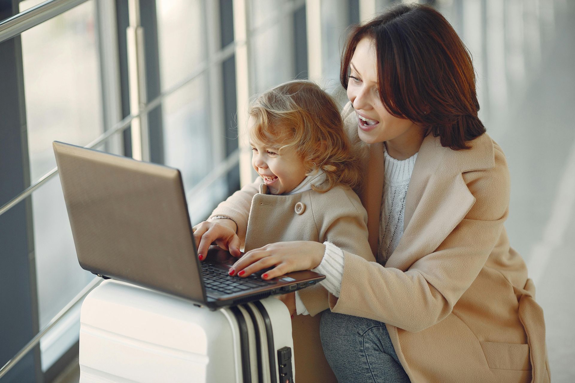 Mother and young child looking at a laptop together with a suitcase, preparing for an international family relocation