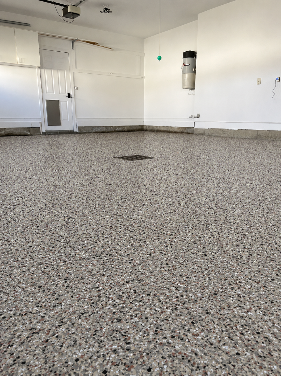 Empty garage with speckled gray floor and white walls, showing a small wall-mounted fixture.