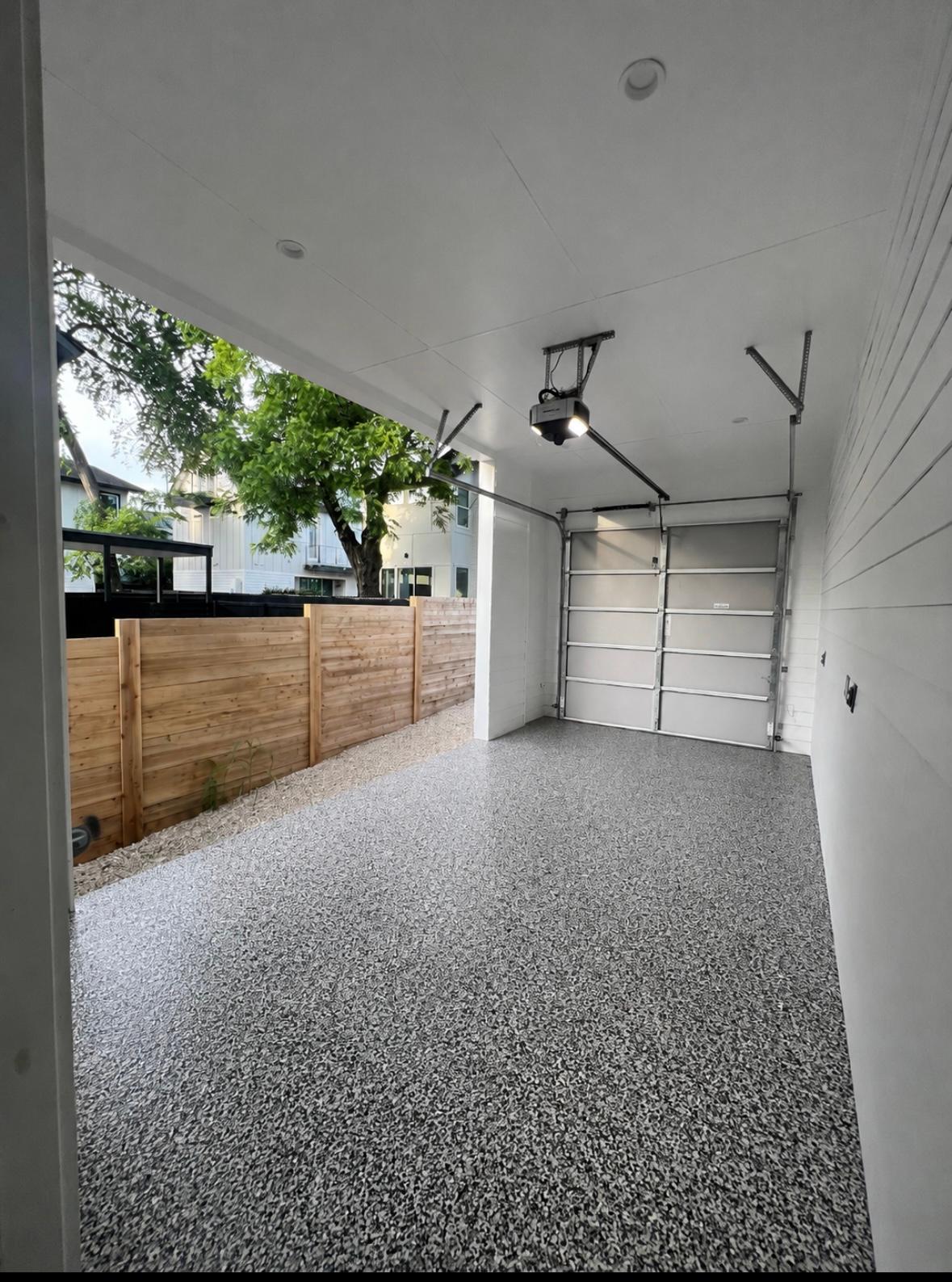 Covered garage with speckled floor, white walls, ceiling fan, and garage door at the far end.