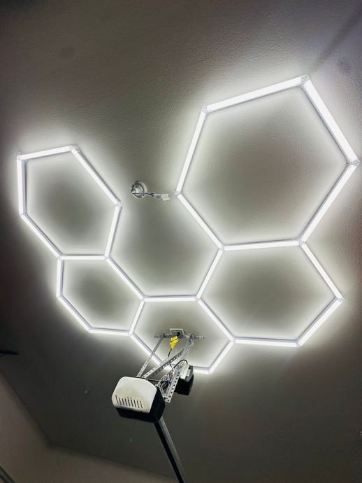 Glowing hexagonal LED wall light panels on a dark ceiling with a small device below