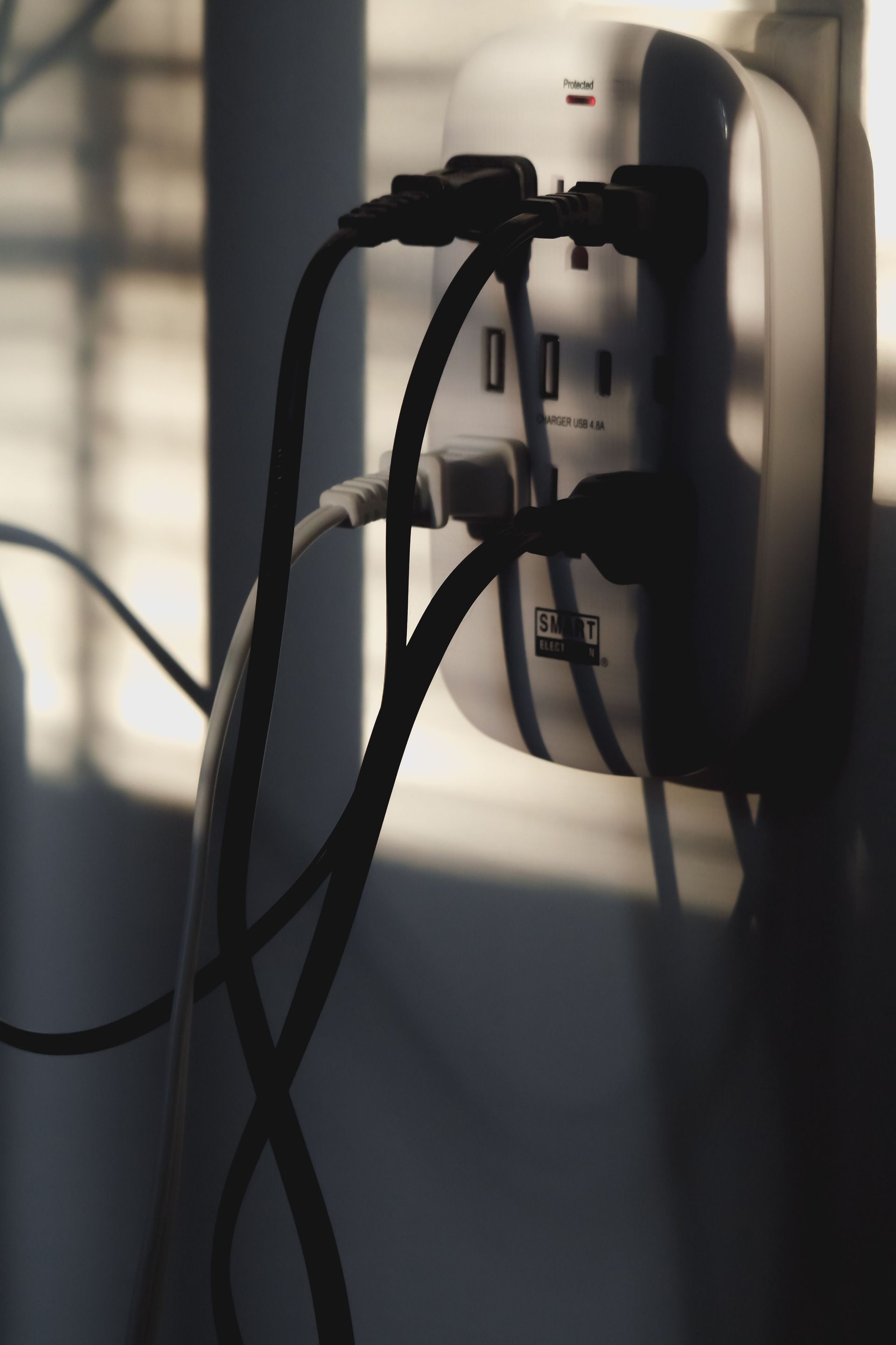Black cables plugged into a wall-mounted power outlet in sunlight.