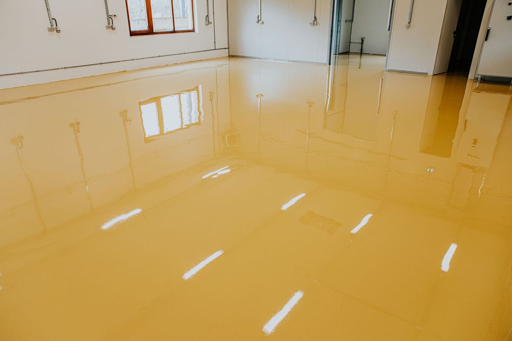 Glossy yellow epoxy floor in a bright, empty room with windows reflecting on the surface