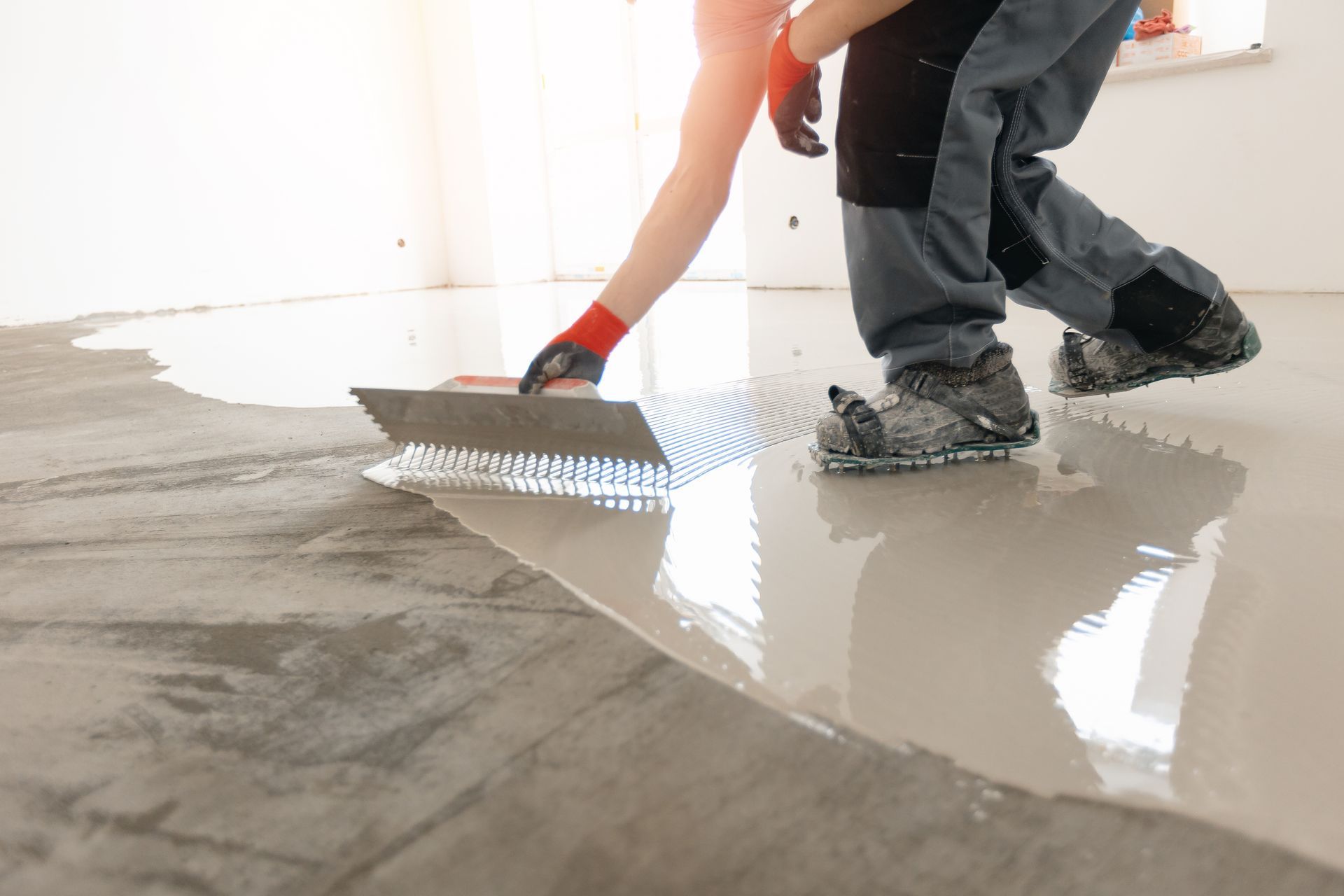 Worker smoothing wet concrete with a trowel on a floor interior