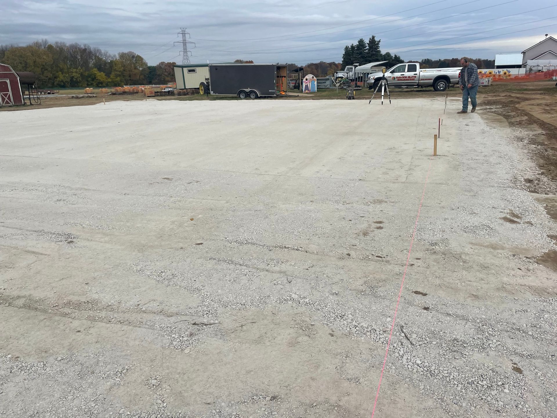 A gravel parking lot under construction with a person and surveying equipment visible.