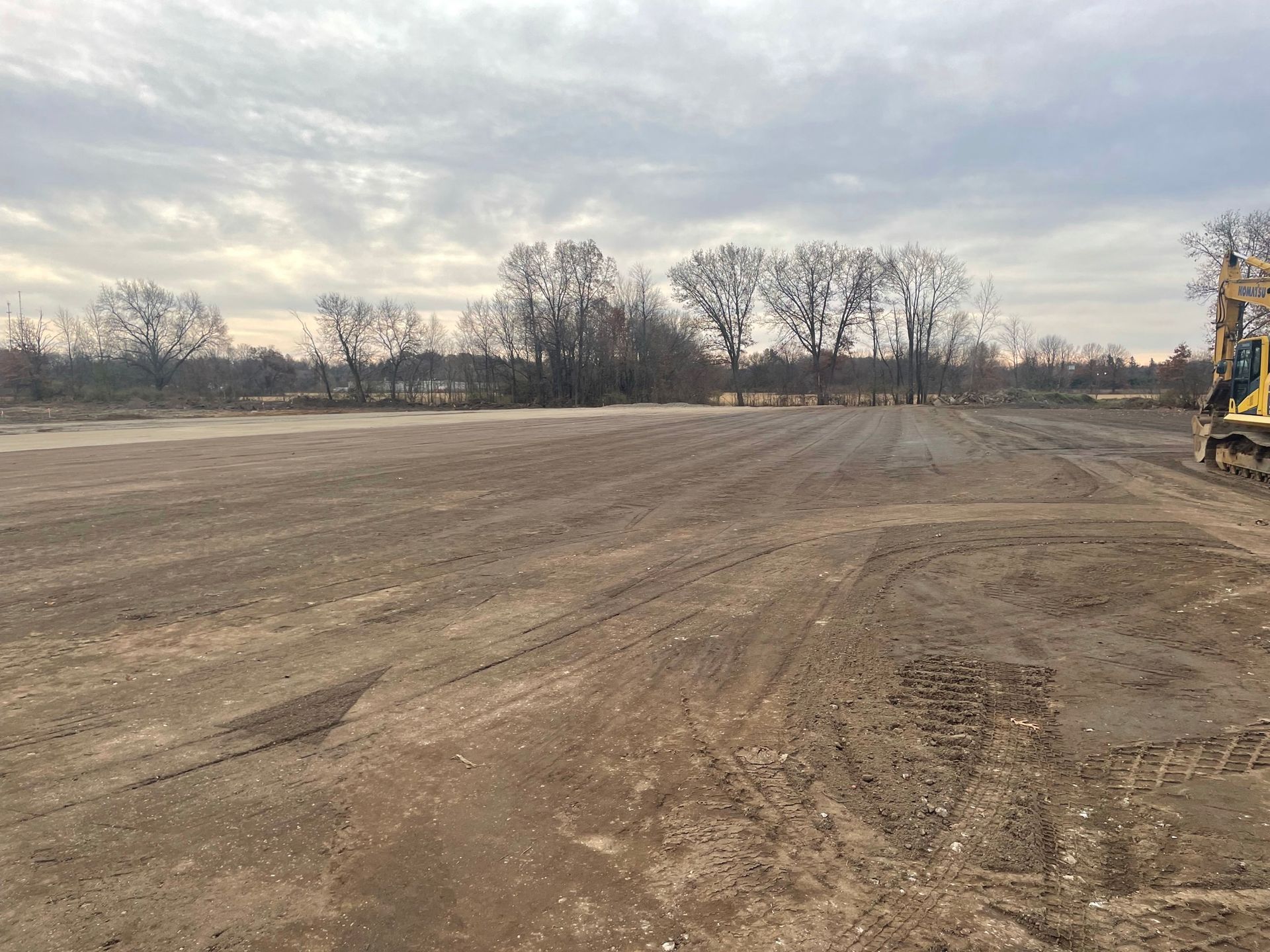 Cleared field, bare trees in the distance, heavy machinery at the right, overcast sky.
