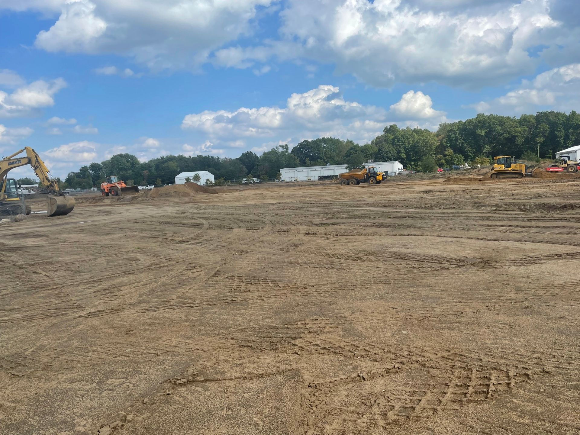 Construction site with heavy machinery on a dirt field under a cloudy blue sky.