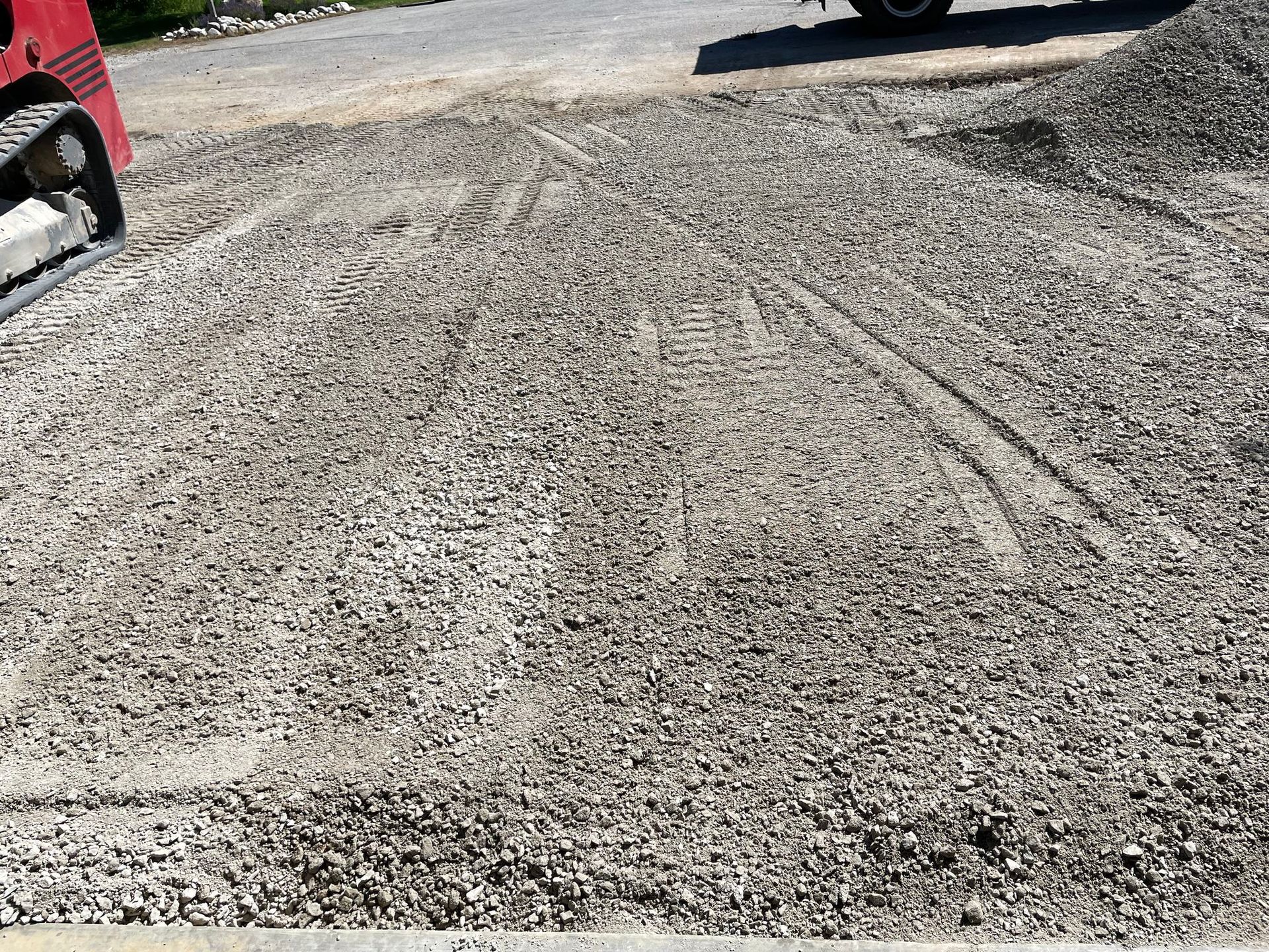 Gravel surface with vehicle tracks. A skid steer loader is on the left.