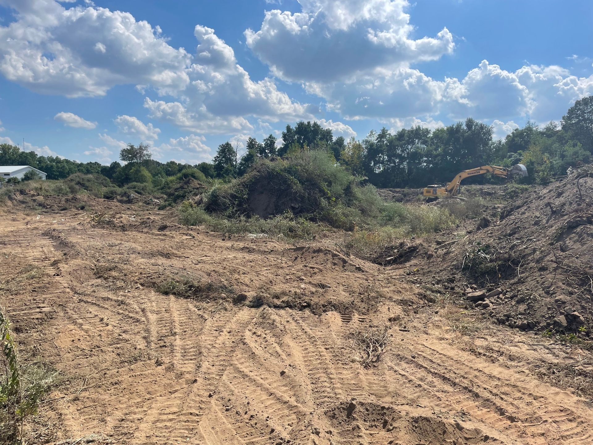 Cleared land with dirt piles and tire tracks under a partly cloudy sky.