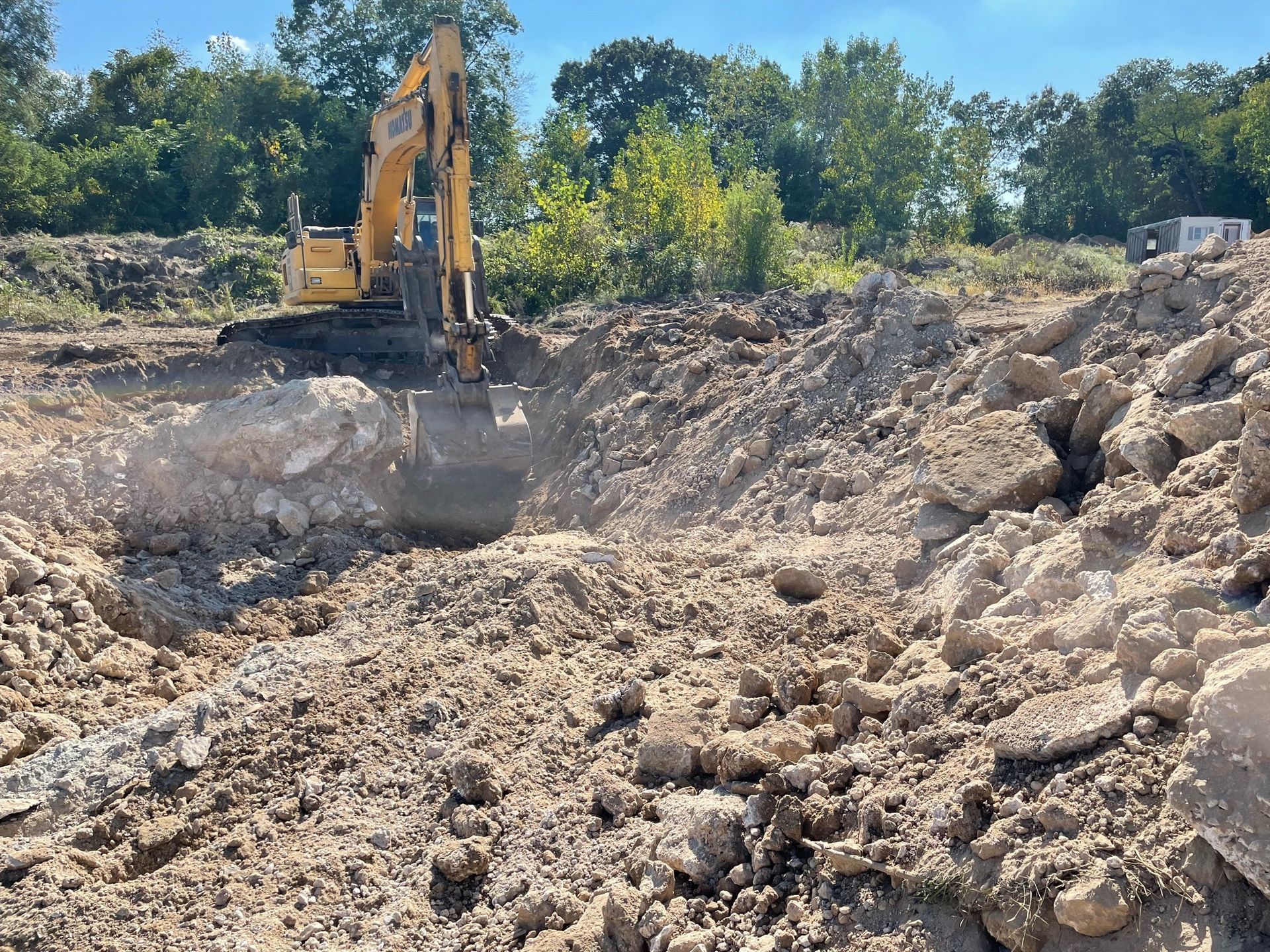 Yellow excavator digging in a dirt and rubble construction site under a blue sky.
