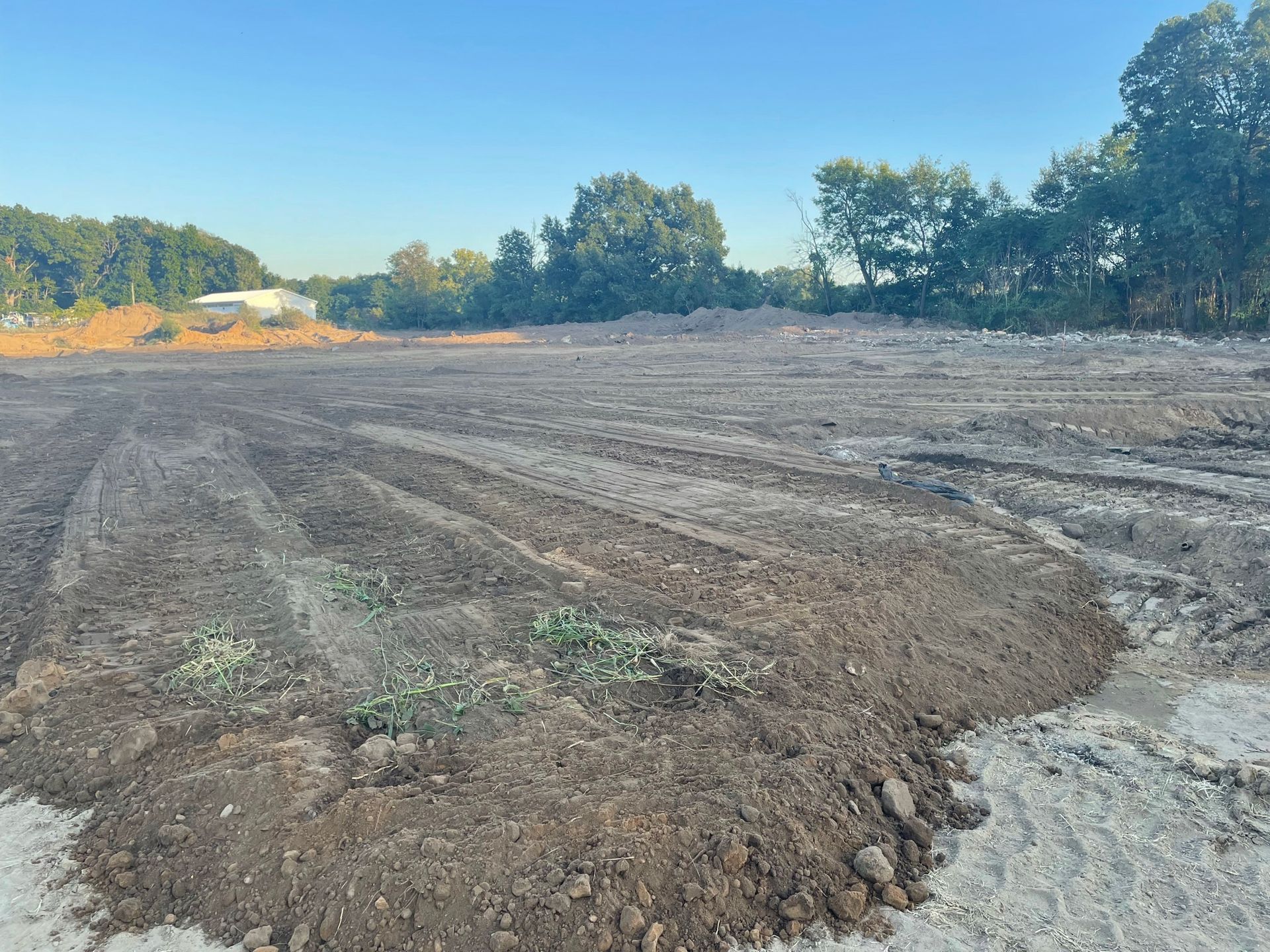Cleared dirt lot with tire tracks, trees in the background, blue sky.