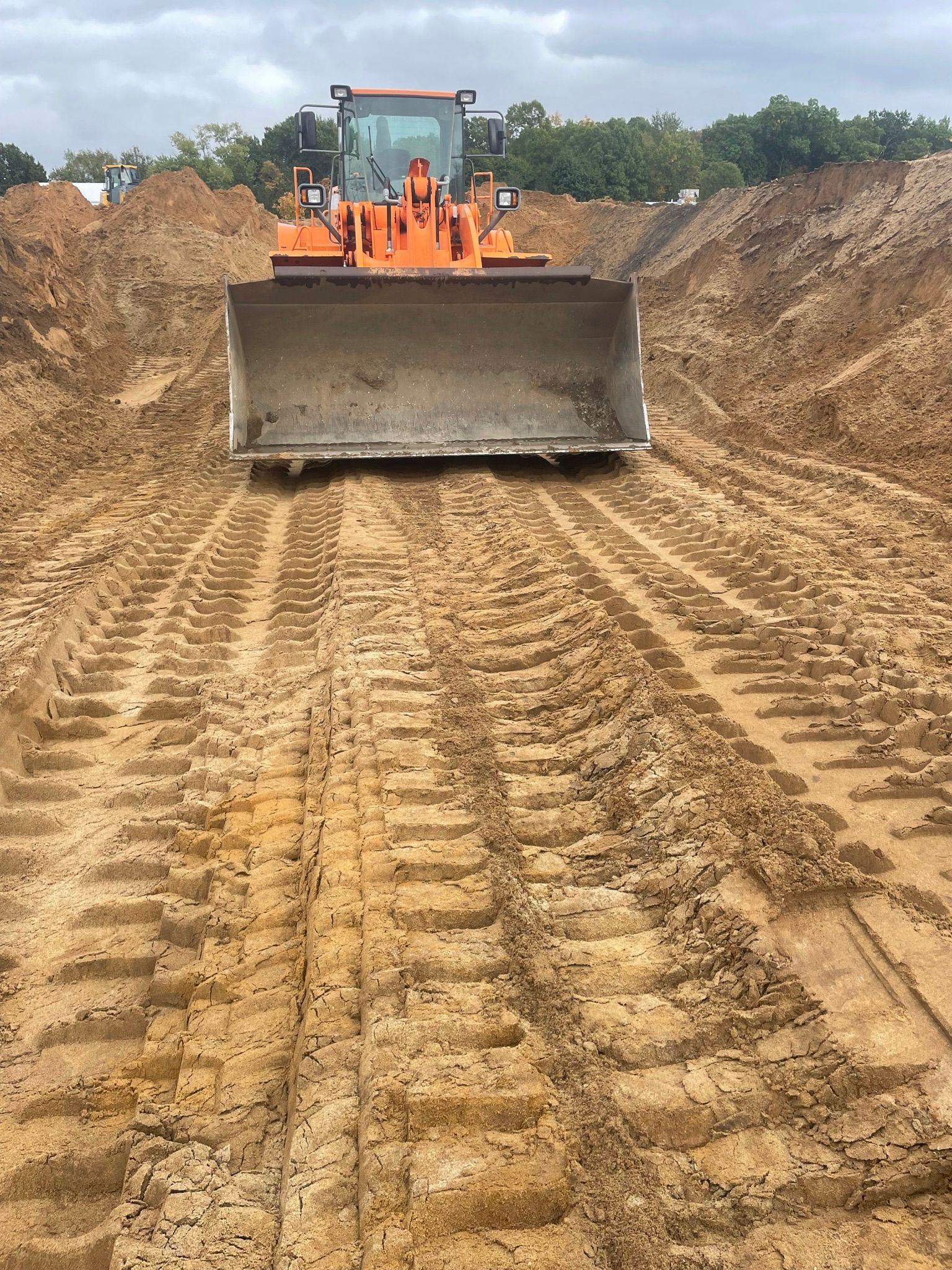 Orange front-end loader on dirt, creating tire tracks. Earth-moving equipment at work.