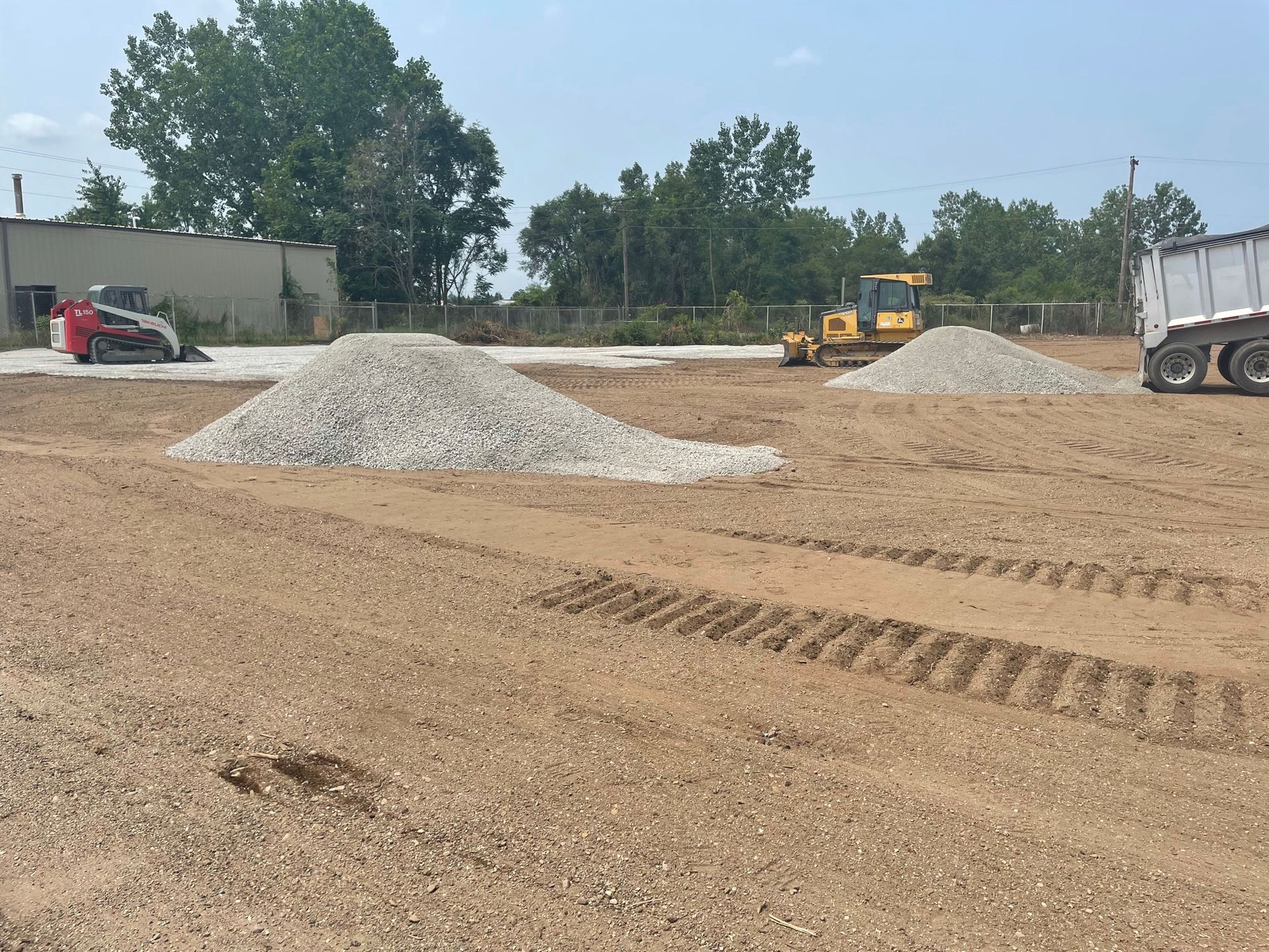 Construction site with piles of gravel, a bulldozer, and a truck on dirt.