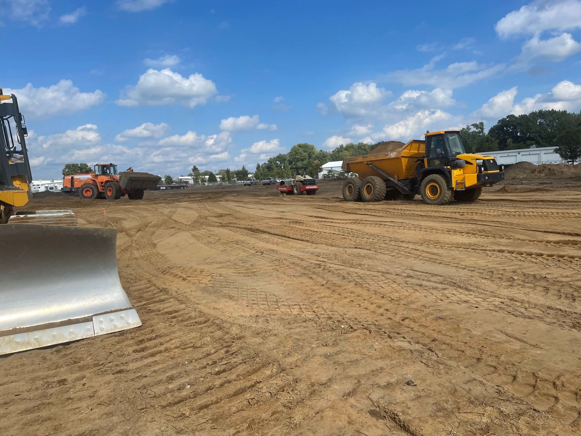 Construction site with heavy machinery, including a dump truck, moving dirt on a sunny day.