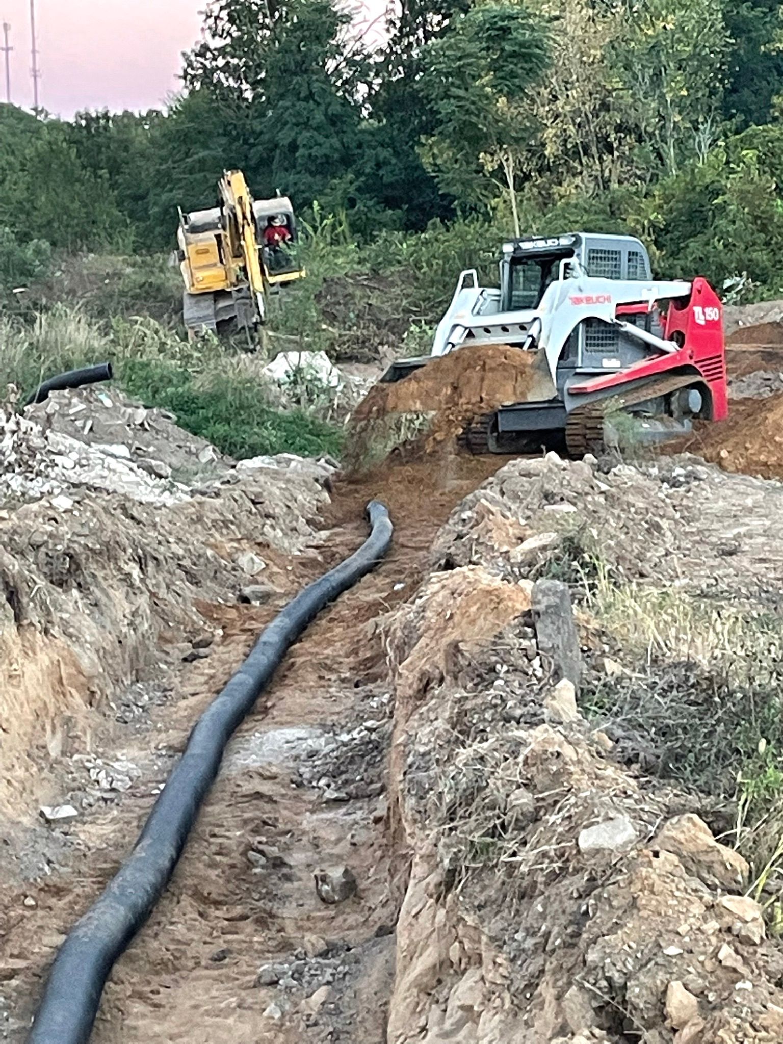 Construction site with a black pipe in a trench, excavator and skid steer.