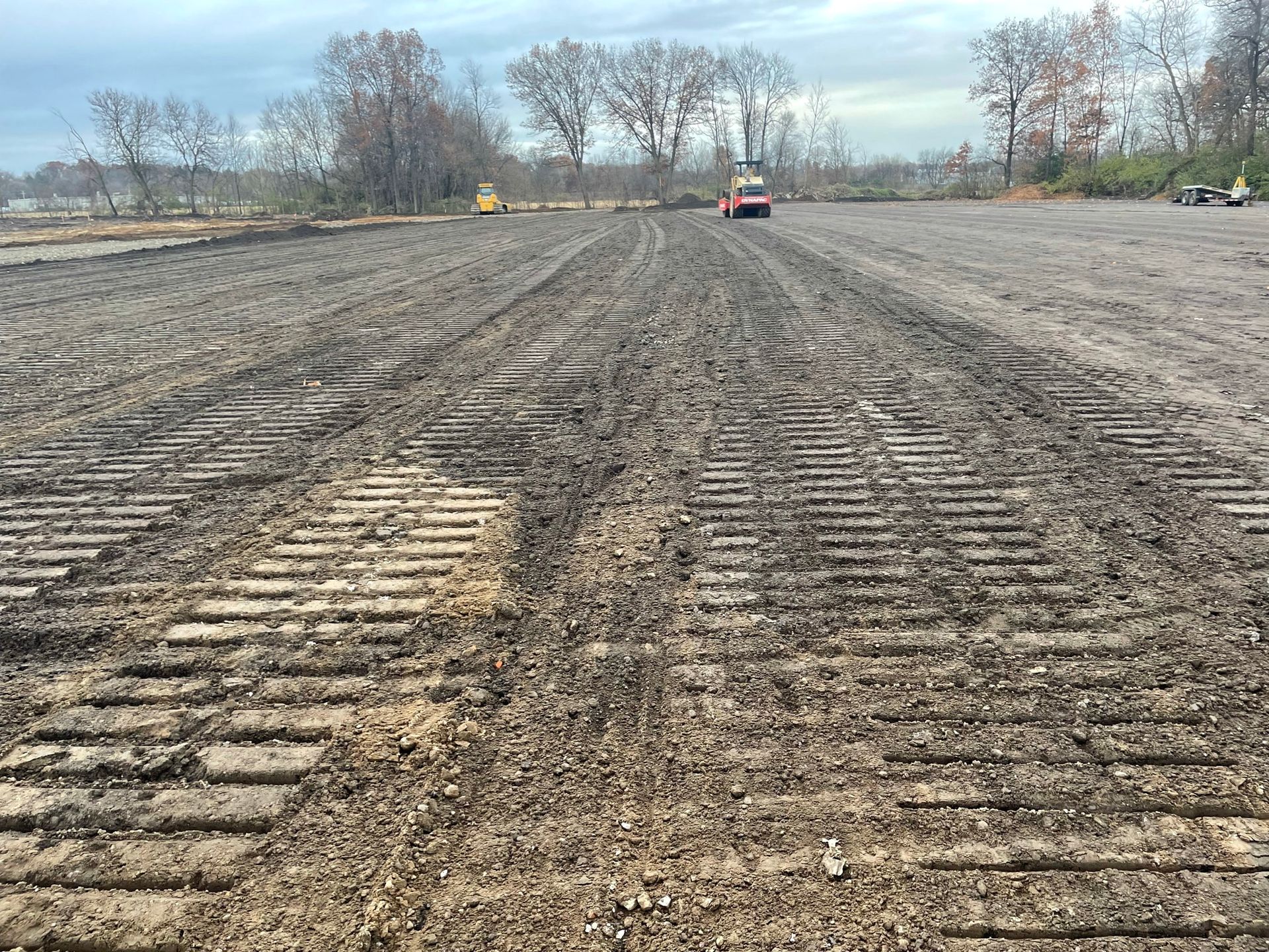 Muddy field with tractor tracks, trees in background, and construction equipment.