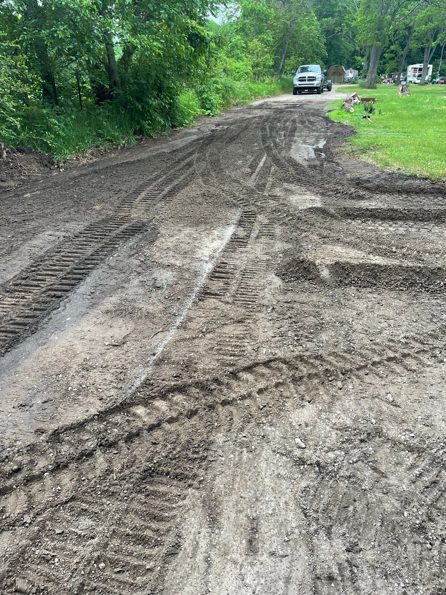 Muddy dirt road with deep tire tracks, vehicle at end, trees in background.