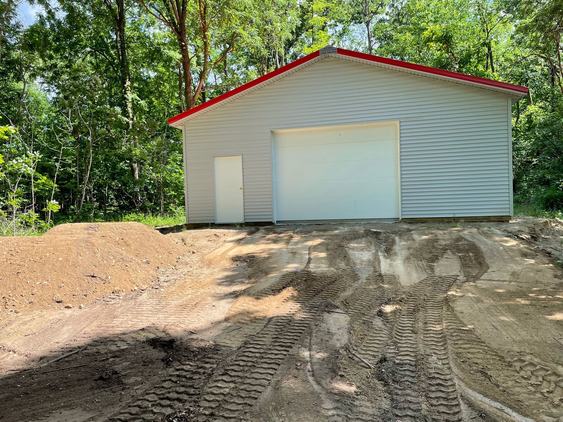 White garage with red trim on a small hill in a wooded area.
