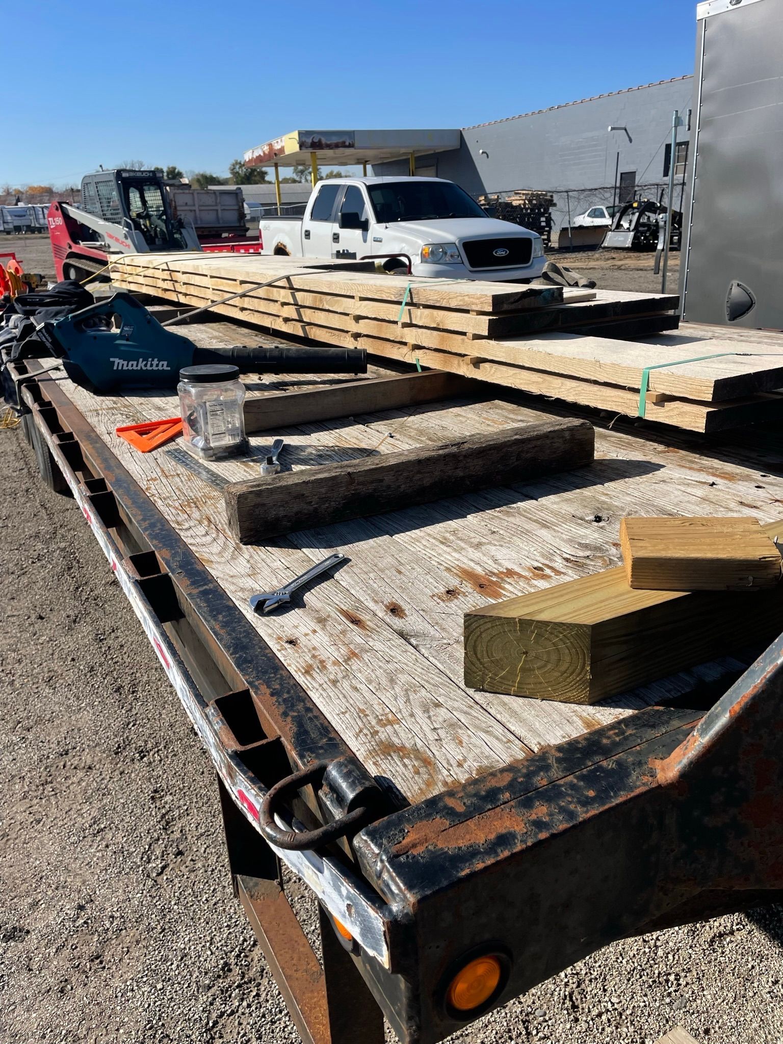 Flatbed trailer loaded with lumber, tools, and insulation blocks, parked outdoors under a sunny sky.