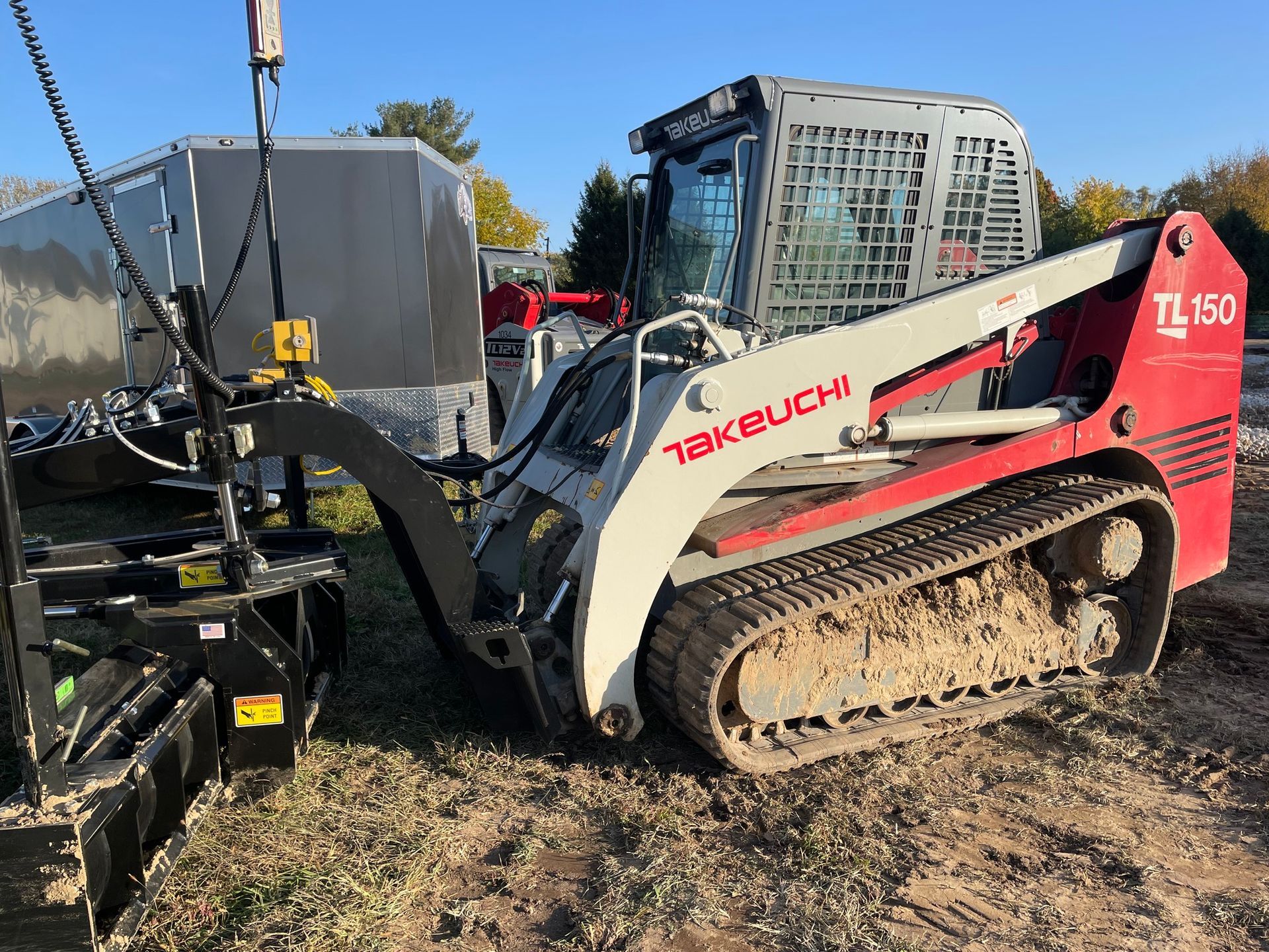 A Takeuchi TL150 track loader in a yard setting with an attached implement.
