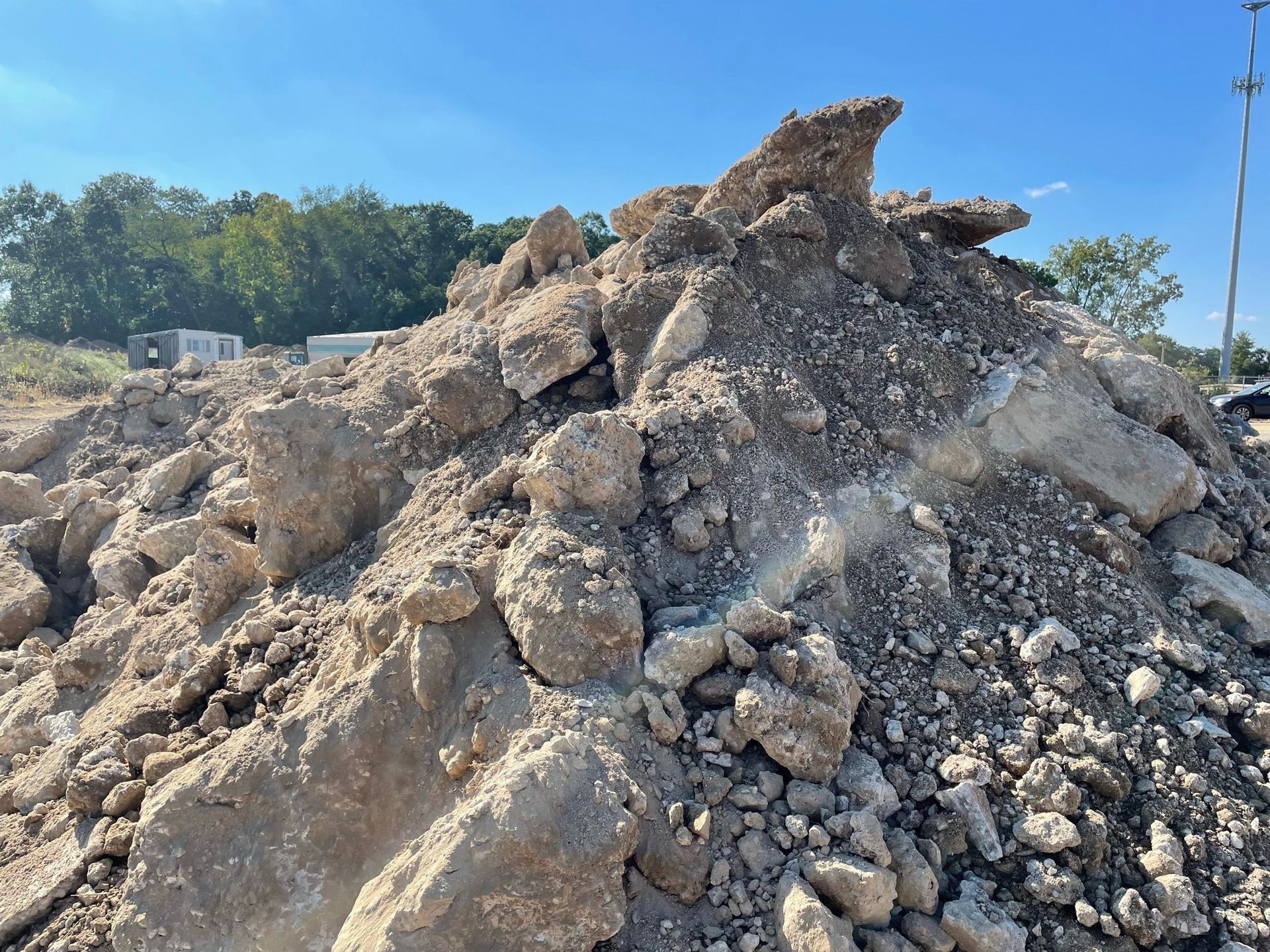 Pile of rubble and dirt on a construction site under a blue sky, with trees in the background.