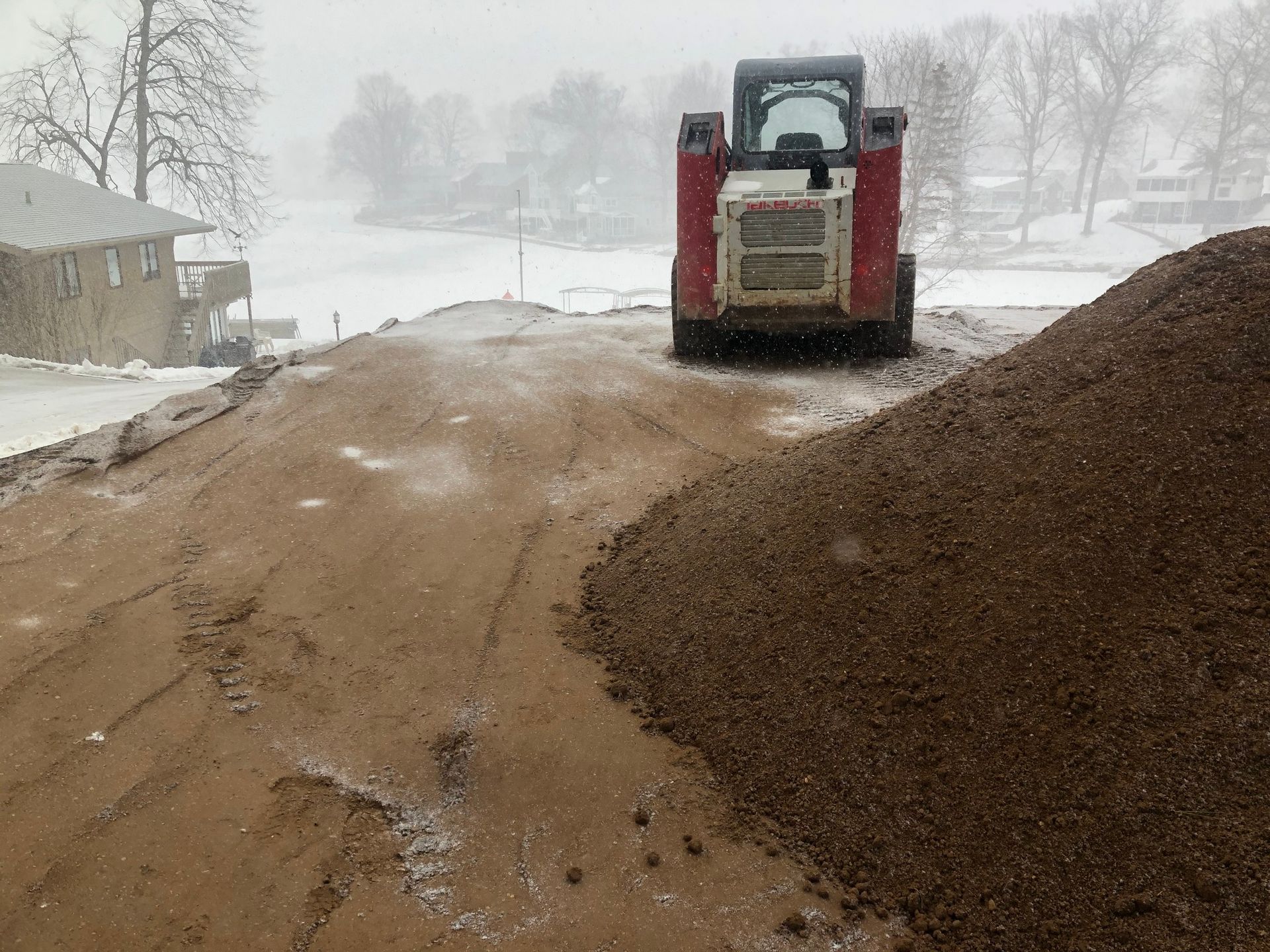 Red skid steer on a dirt pile, snowy landscape background.