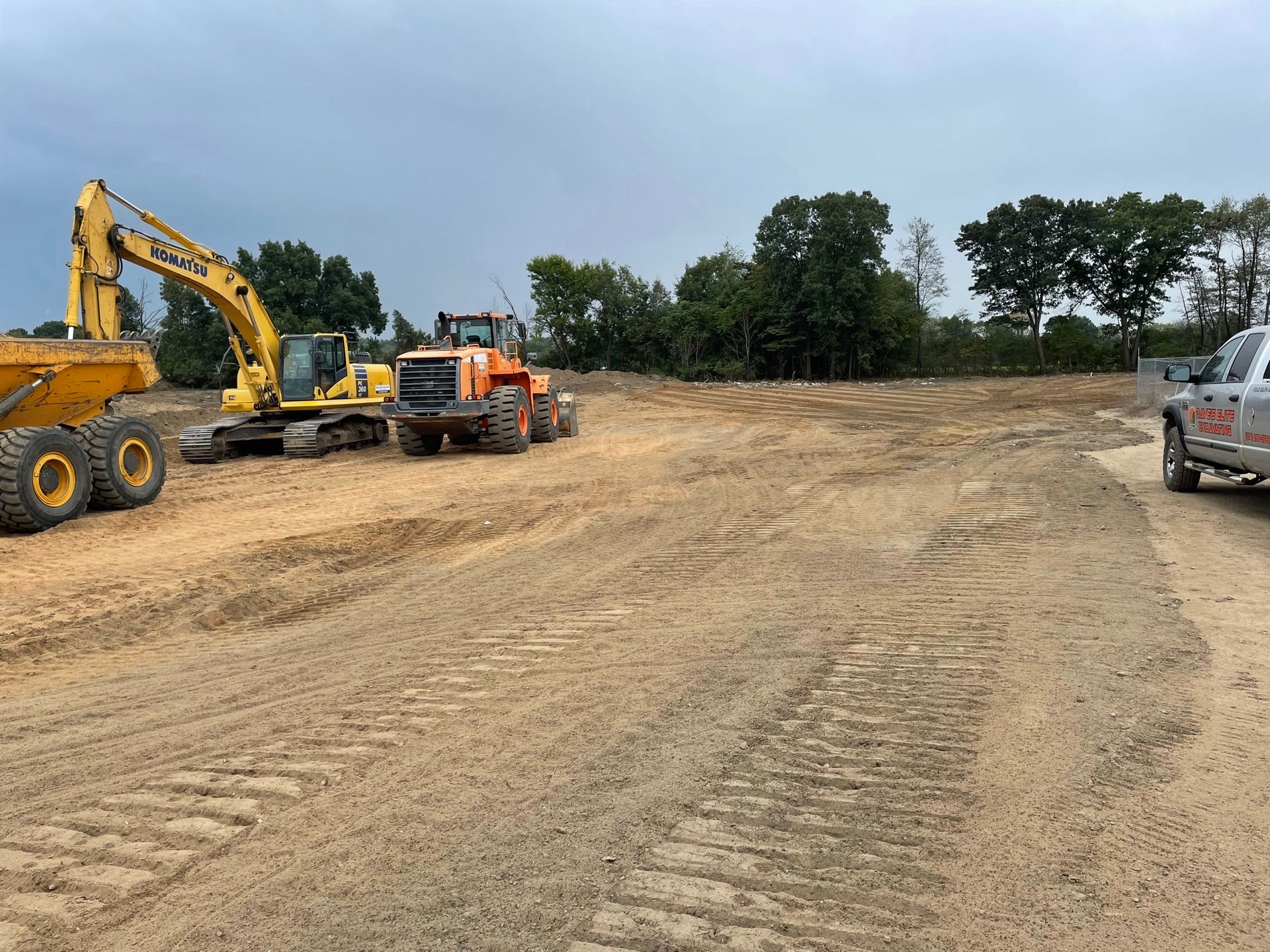 Construction site with heavy machinery on a cleared area under cloudy skies.