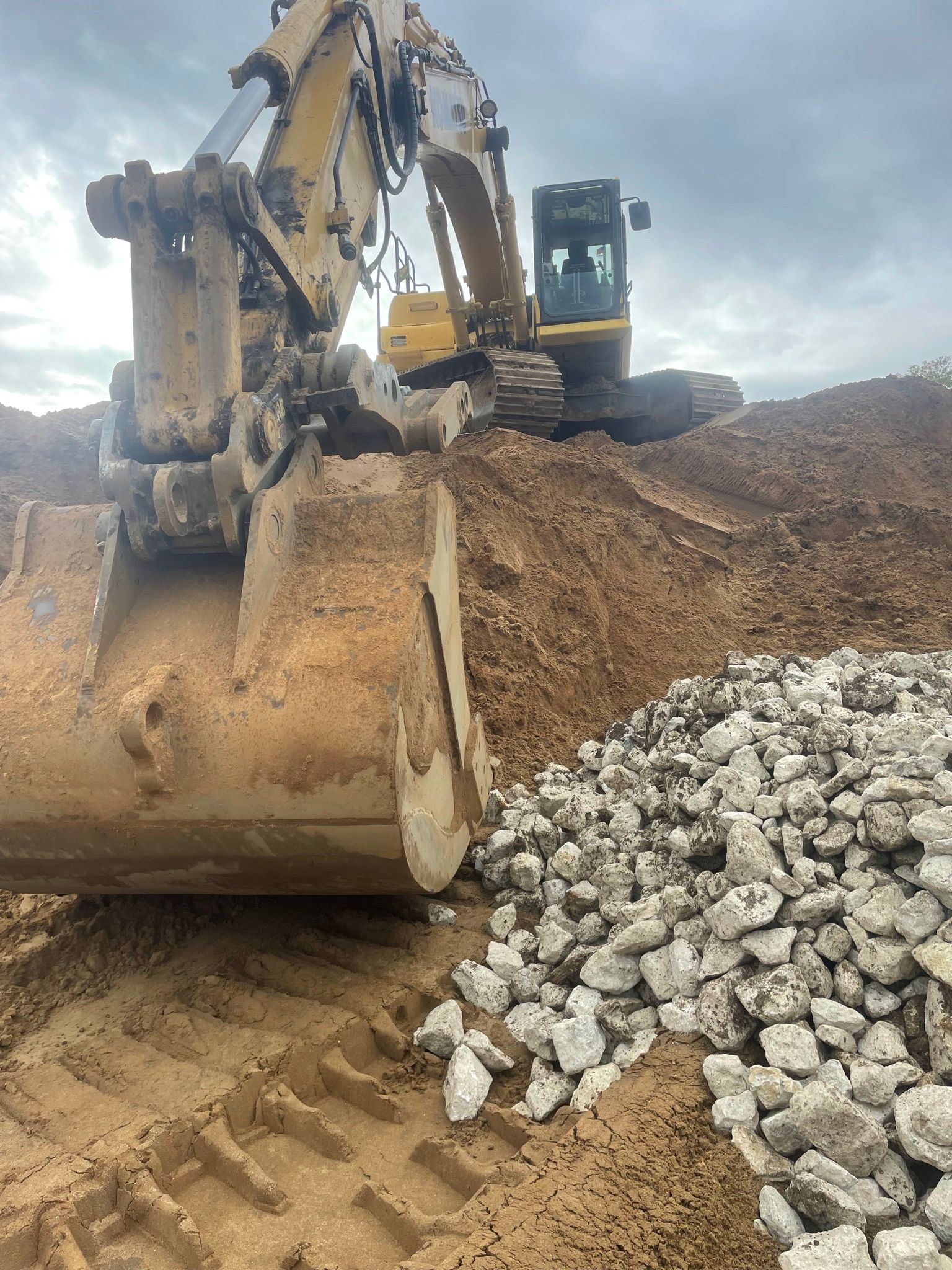 Excavator scooping rubble at a construction site. Bucket in foreground, earth pile behind.