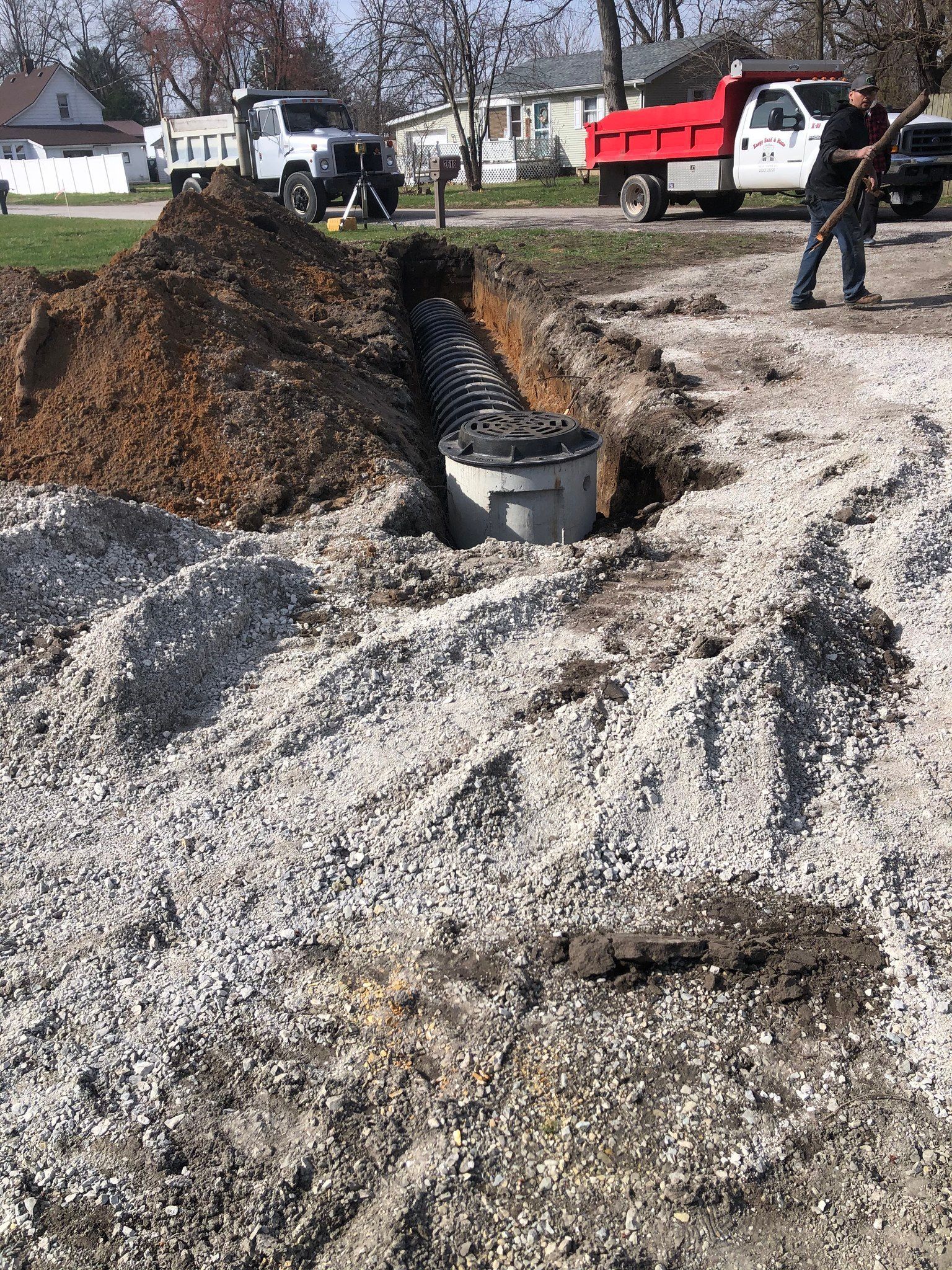 Construction site: a septic tank installation in progress. Trucks, gravel, and a worker near the tank.