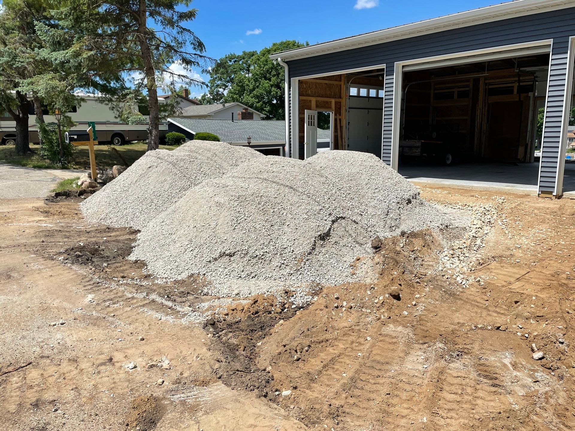Gravel piles in front of a blue garage under construction on a sunny day.