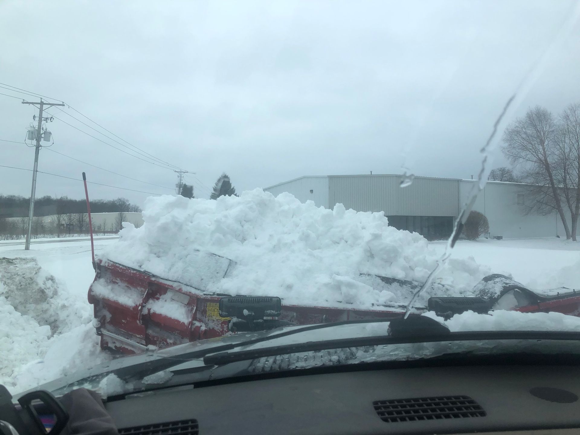 Snowplow pushing a large pile of snow, cloudy day, industrial setting.