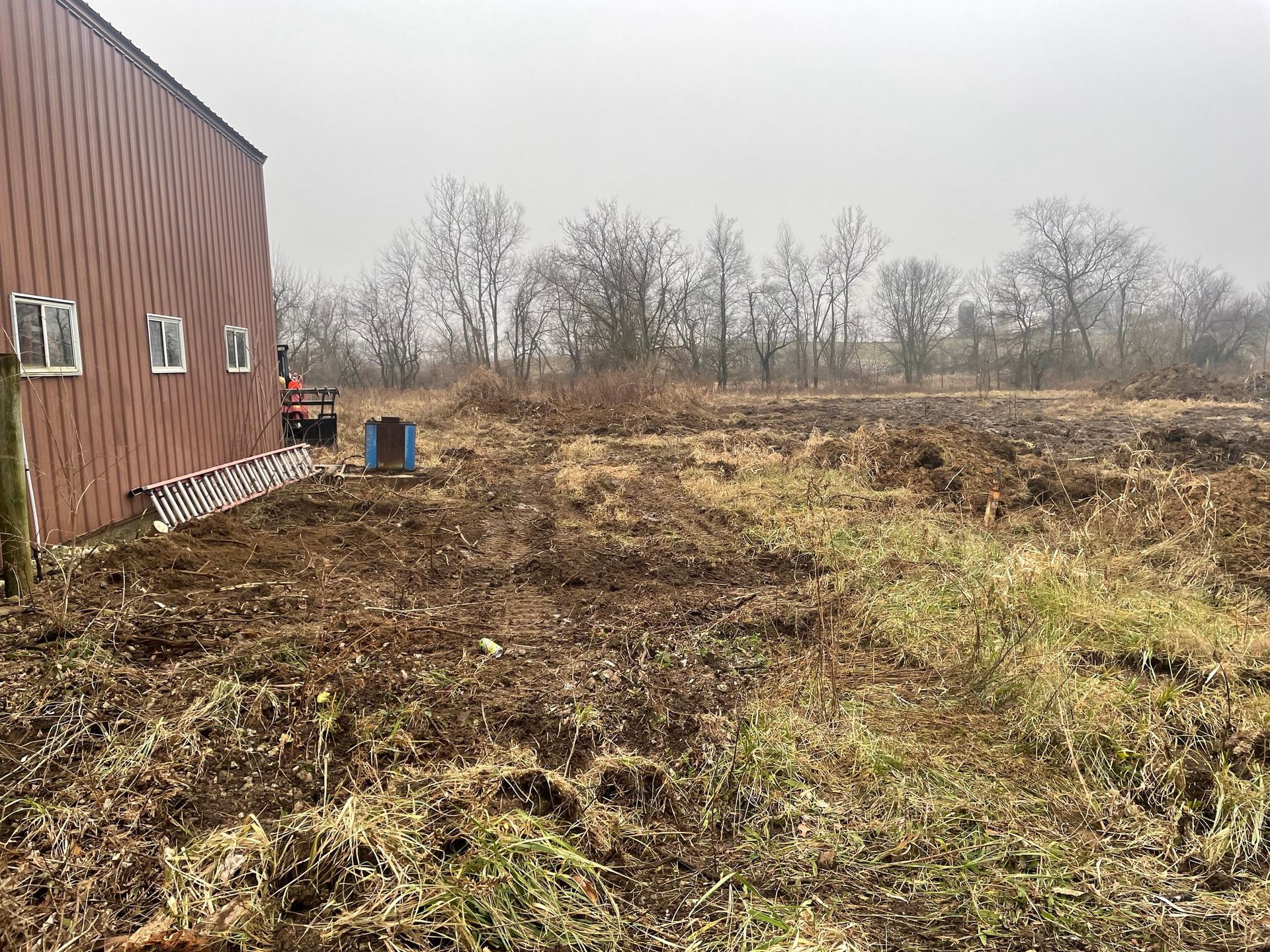 Brown building next to a cleared field with dead vegetation under an overcast sky.