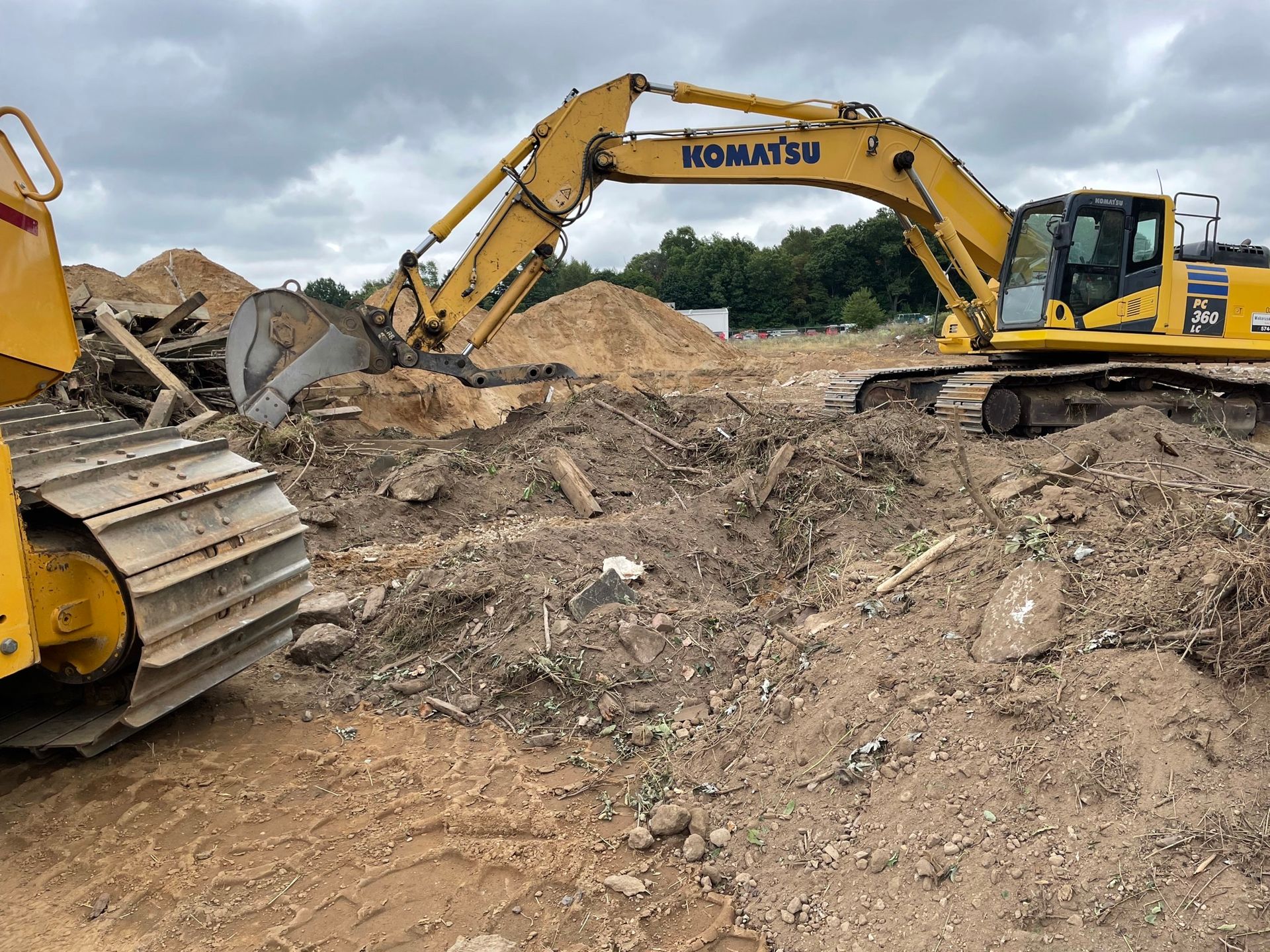 Yellow bulldozer and excavator on a construction site, moving dirt and debris under an overcast sky.