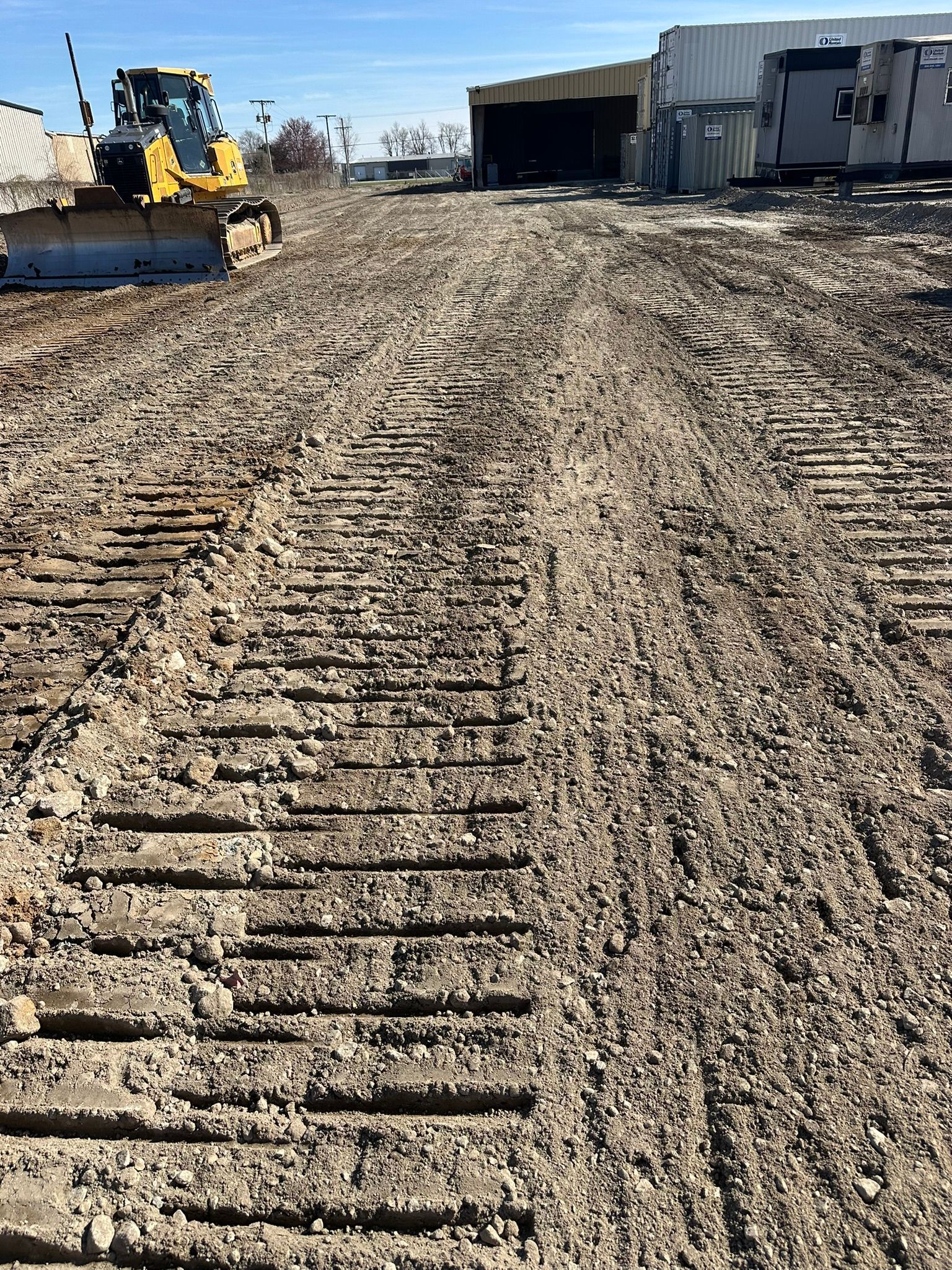 Muddy construction site with bulldozer and storage containers.
