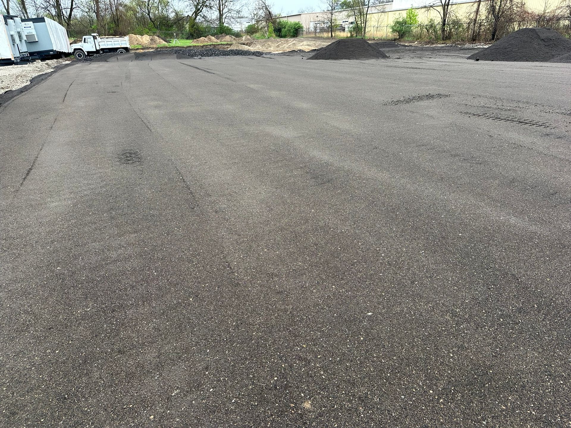 Asphalt parking lot with dark gray surface and piles of gravel in the distance.