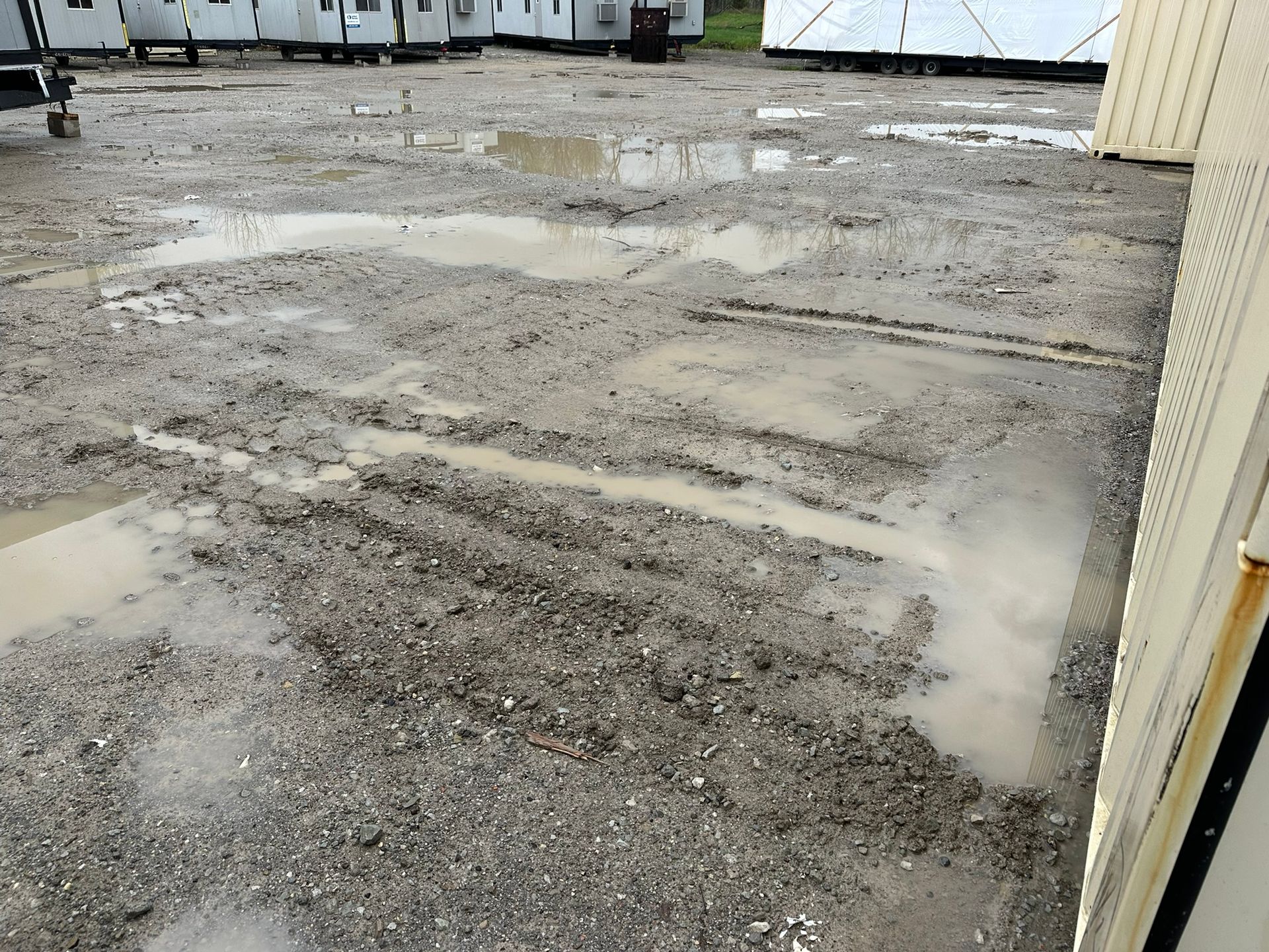 Muddy gravel lot with puddles; modular buildings in the background.