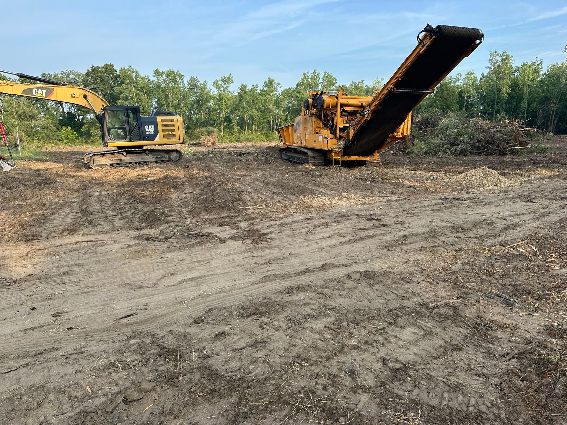 An excavator and wood chipper processing brush in a cleared, outdoor area.