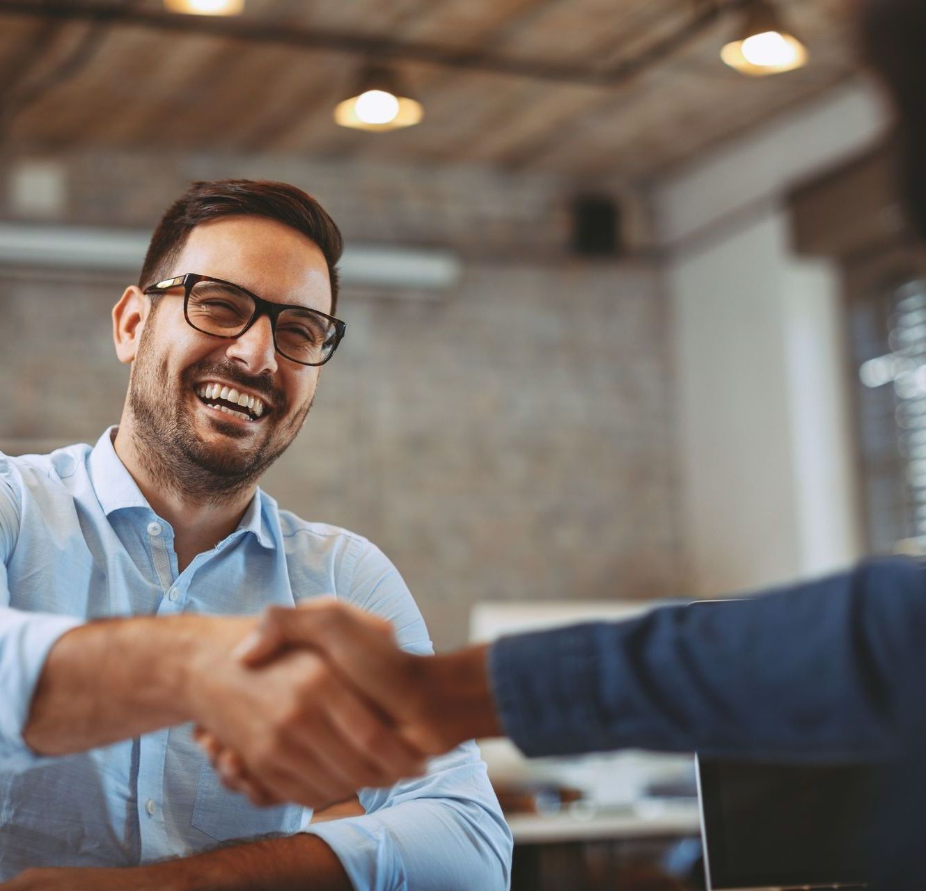 A man wearing glasses is shaking hands with another man.