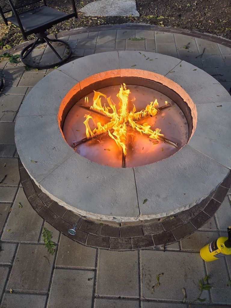 Outdoor patio with stone fire pit, seating, and covered porch under blue sky.