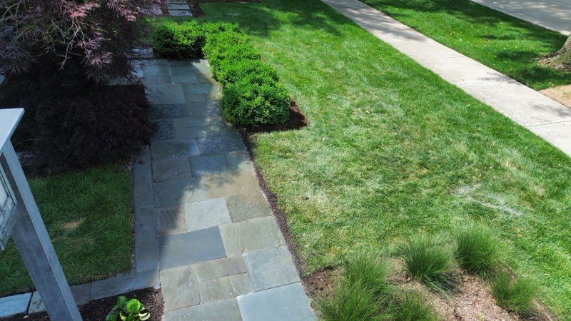 Patio with pergola, seating, and landscaping; artificial turf lawn, stone walkway. 